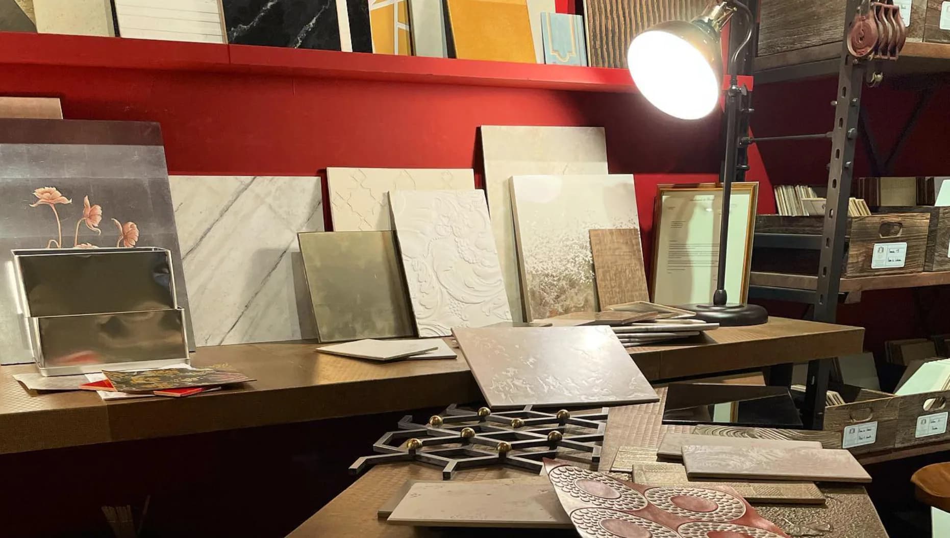 Design studio workspace with red beam overhead, drafting table, material samples, sketches, and mood boards displayed on wall by Atelier Premiere.