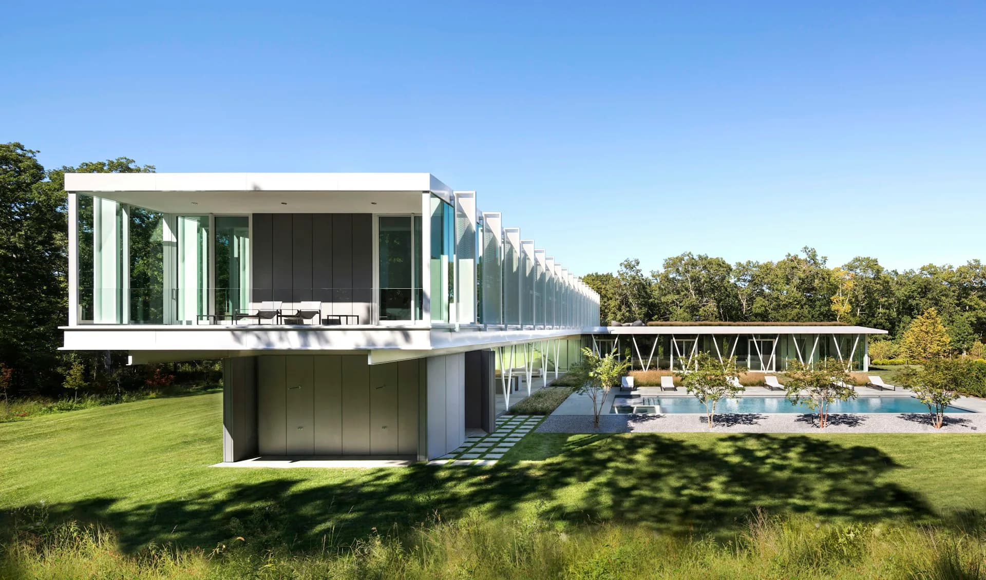 Modern cantilevered house with steel frame and glass walls overlooking manicured lawn and pool, surrounded by trees by Audrey Matlock Architect.
