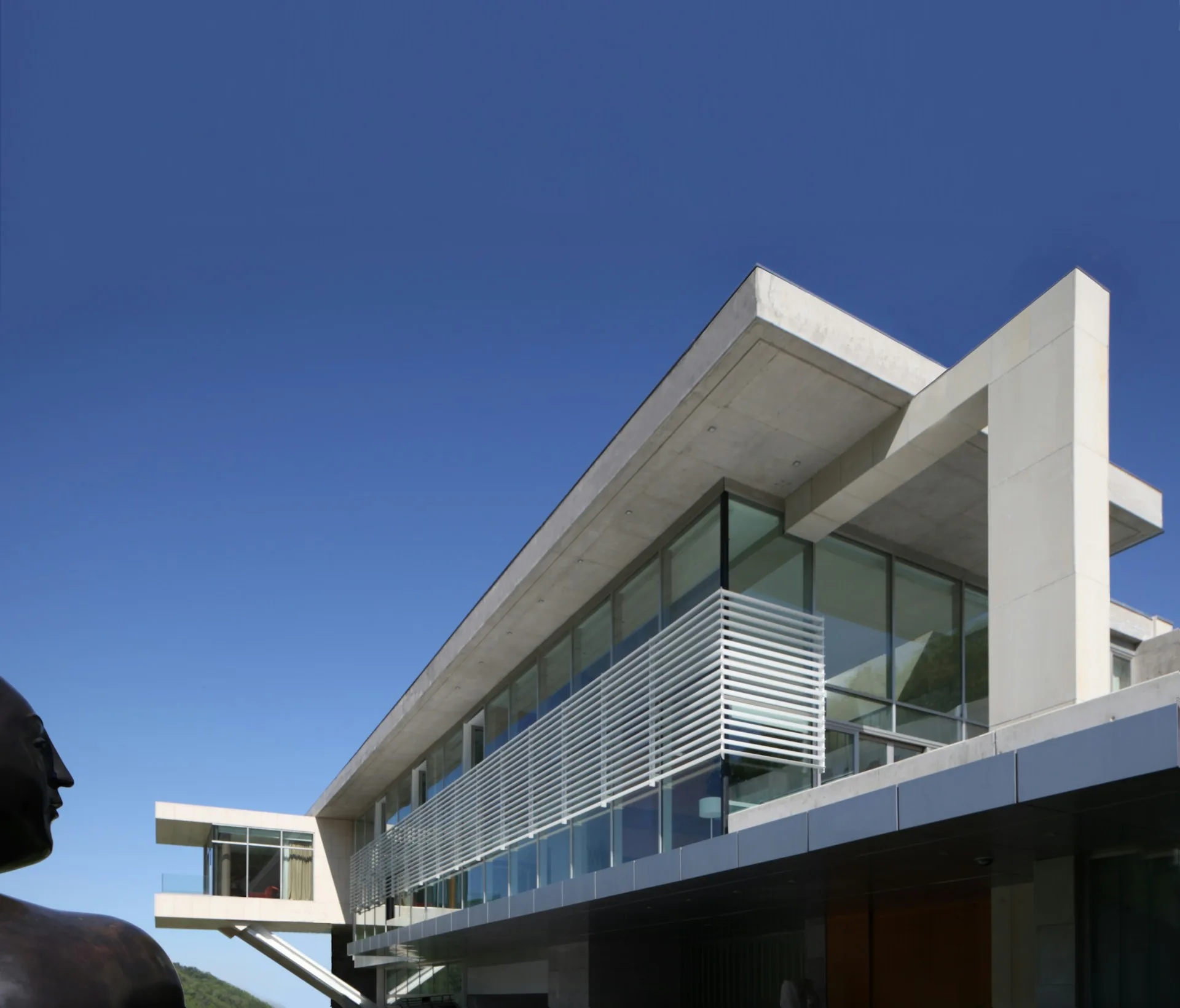 Modern white concrete residential building with horizontal metal louver screening, extensive glazing, and cantilevered design against clear blue sky, by Audrey Matlock Architect.