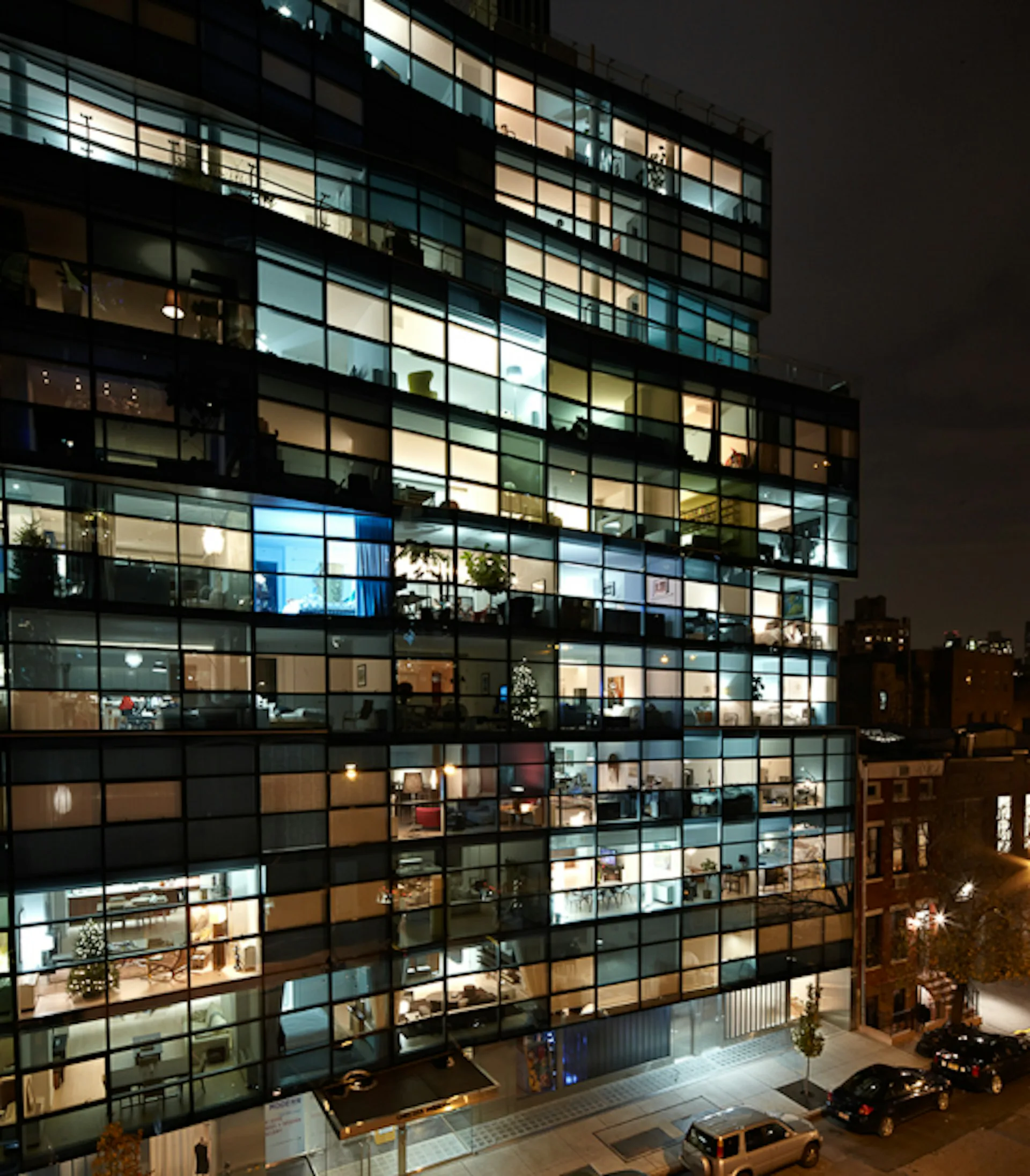 Night photograph of a modern glass-façade office building with illuminated interior spaces across multiple floors, featuring a gridded window pattern and warm lighting throughout, by Audrey Matlock Architect.