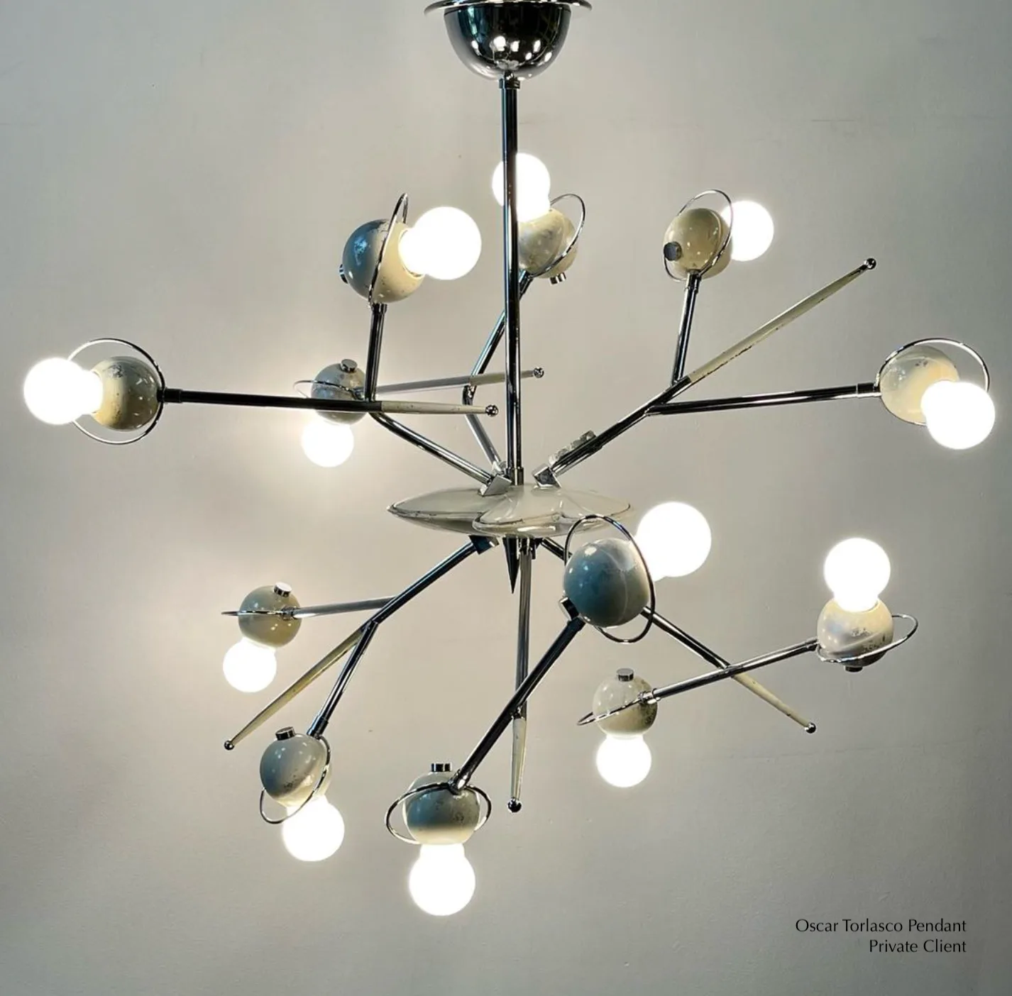 Modern chandelier with chrome central column and multiple articulating arms featuring spherical frosted glass shades and brass accents by Aurora Lampworks.