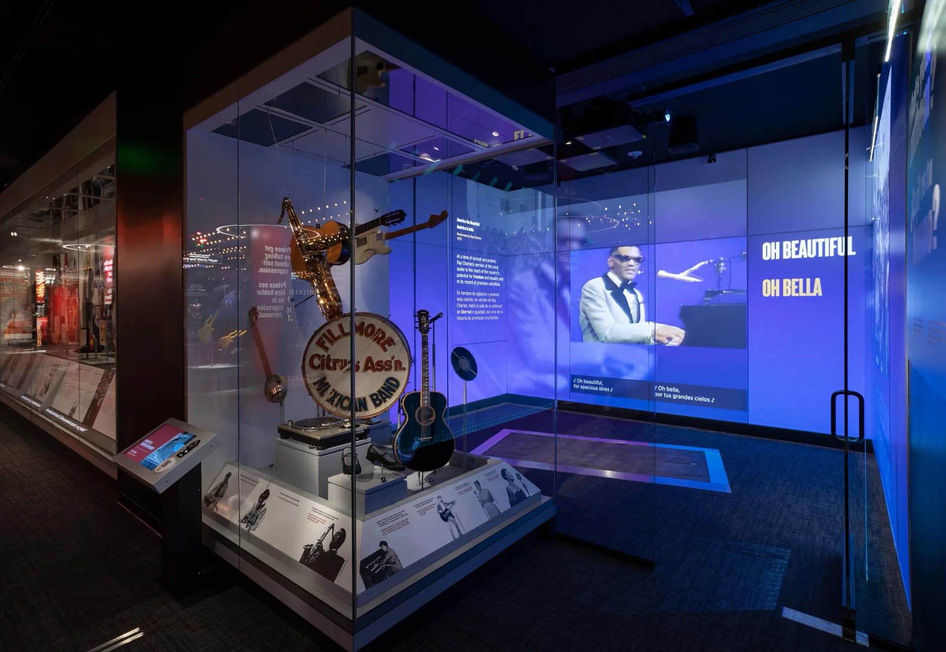 Museum exhibition display with illuminated blue glass cases showcasing vintage bicycle and memorabilia, dramatic lighting and multimedia screens, designed by Available Light.