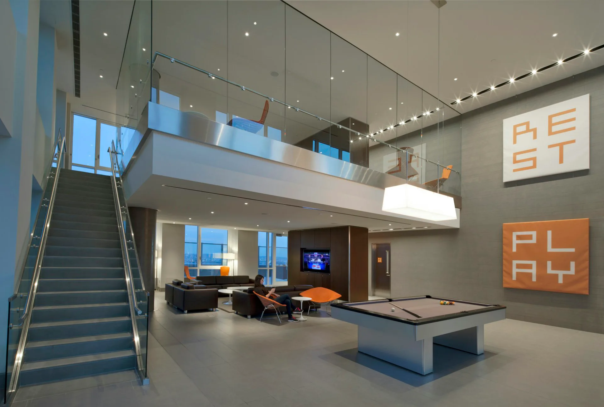 Modern loft interior with mezzanine level, concrete floors, steel staircase, and orange graphic wall signage by Avinash K. Malhotra Architects (AKM).