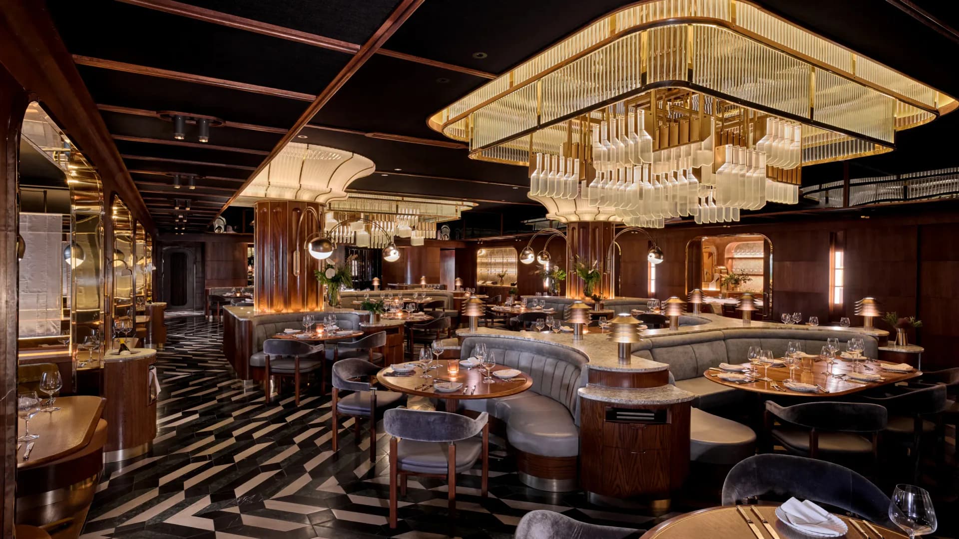 Luxurious restaurant interior with dark wood, geometric black-and-white flooring, dramatic chandelier, and curved banquettes by AvroKO.