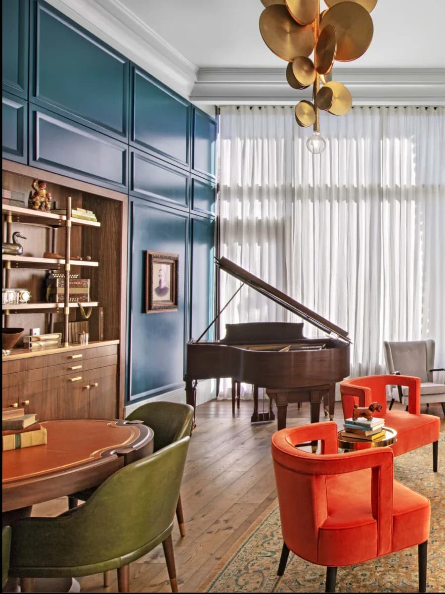 Luxury residential living room featuring teal cabinetry, grand piano, curved red-orange seating, and brass sculptural chandelier by AvroKO.