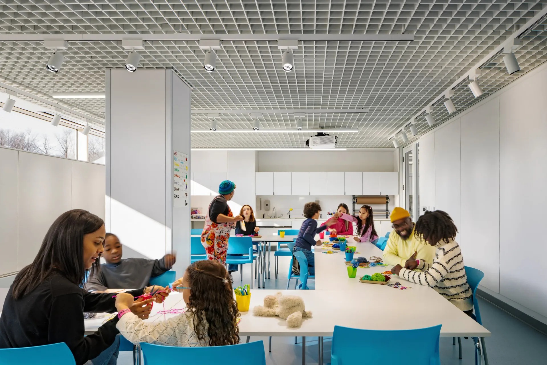 Bright, modern educational space with white walls, blue chairs, and natural lighting features colorful learning areas and multiple children engaged in activities, designed by AYON Studio Architecture and Preservation.