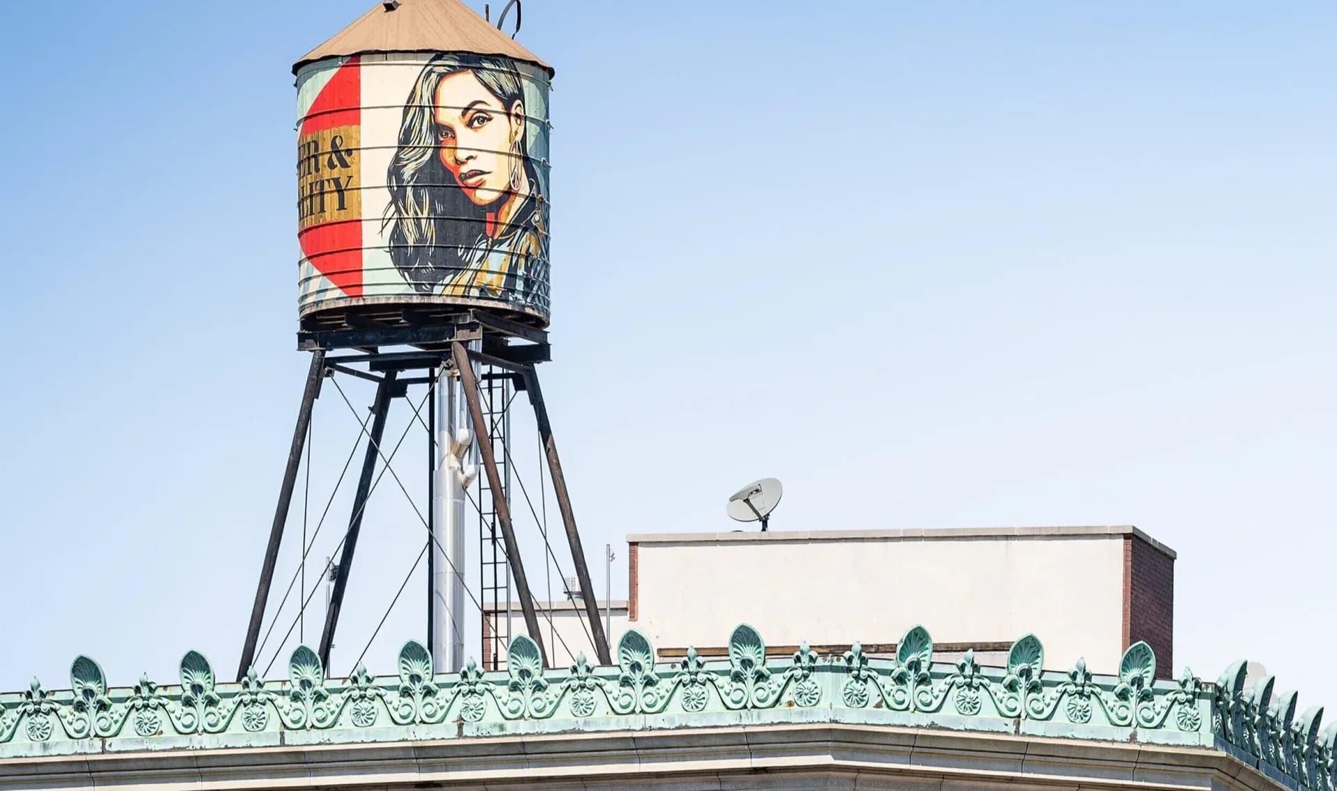 Iconic rooftop water tower with portrait mural and ornamental cornice detail against clear sky, a landmark architectural preservation by AYON Studio Architecture and Preservation.