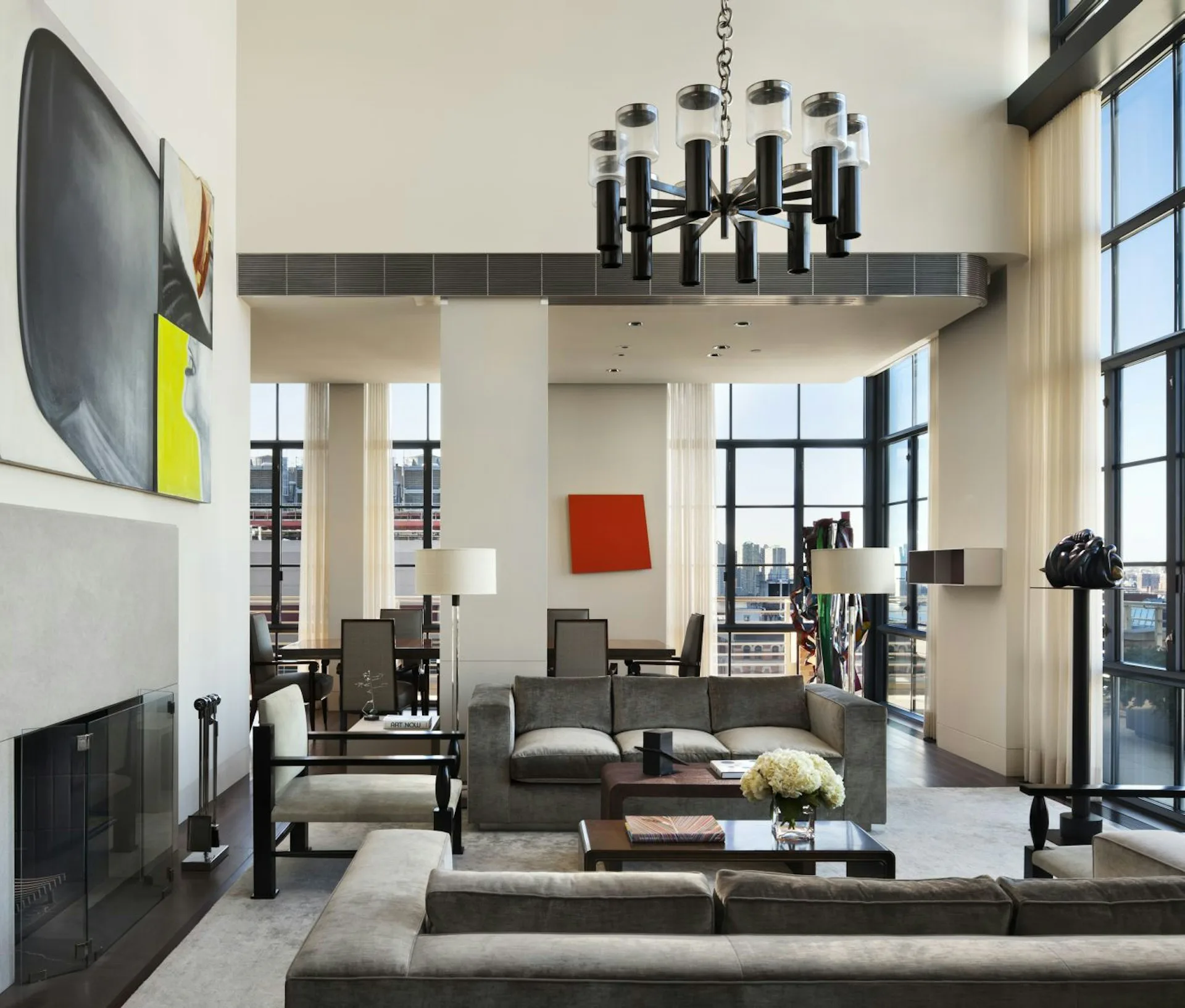 A double-height loft living room with soaring ceilings, charcoal and cream palette, modern black chandelier, floor-to-ceiling windows, and contemporary furnishings by BarlisWedlick Architects LLC.
