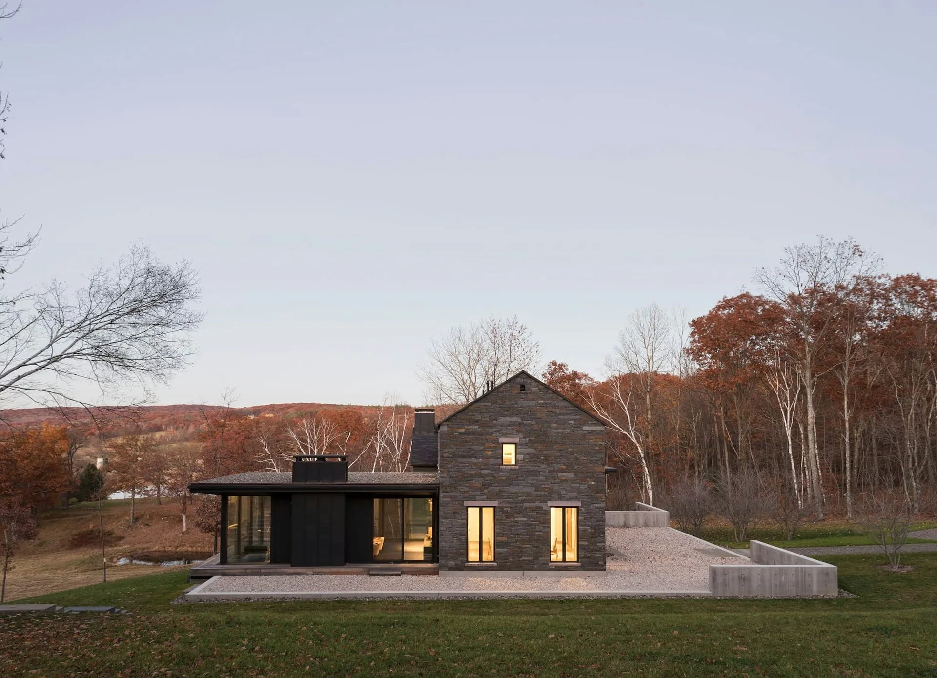 Modern black and glass residential addition attached to a traditional dark barn structure set in a rural landscape with autumn foliage by BarlisWedlick Architects LLC.