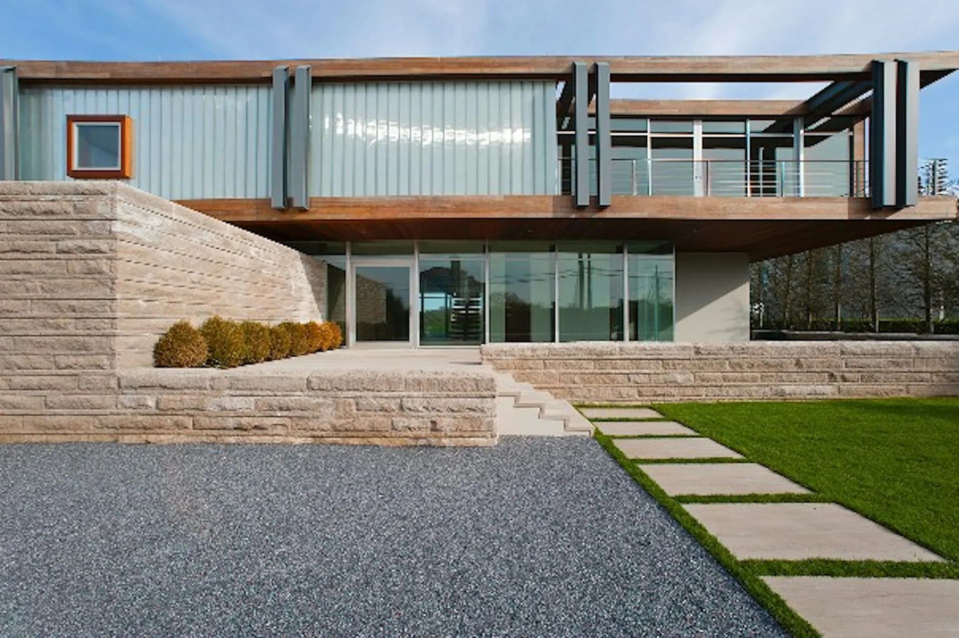 Contemporary residence with stone base, steel frame upper structure, and expansive glazing overlooking manicured lawn and gravel courtyard by Barnes Coy Architects.