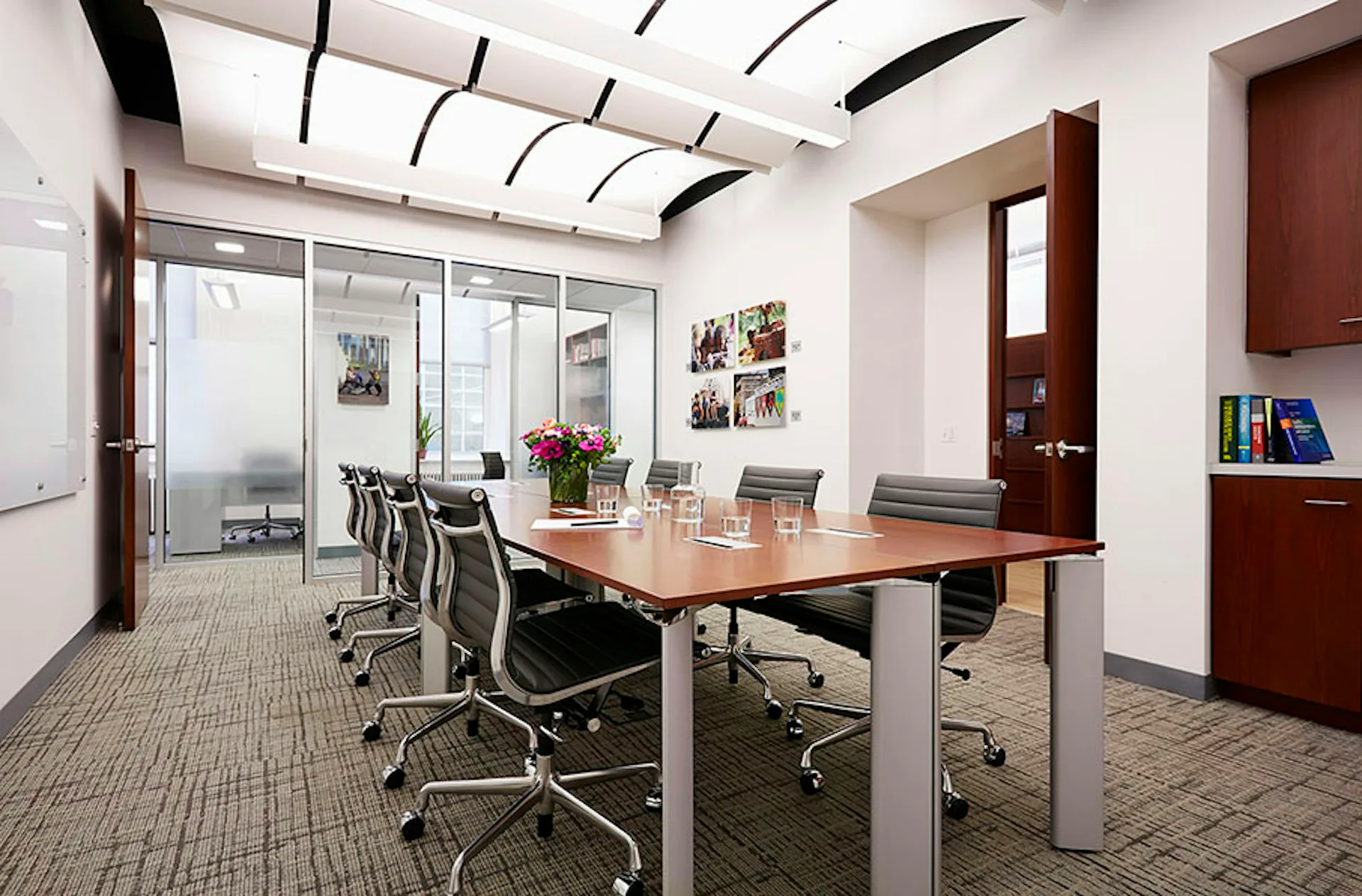 Modern conference room with wood table, black chairs, glass partition walls, and minimalist ceiling detail by Belmont Freeman Architects.