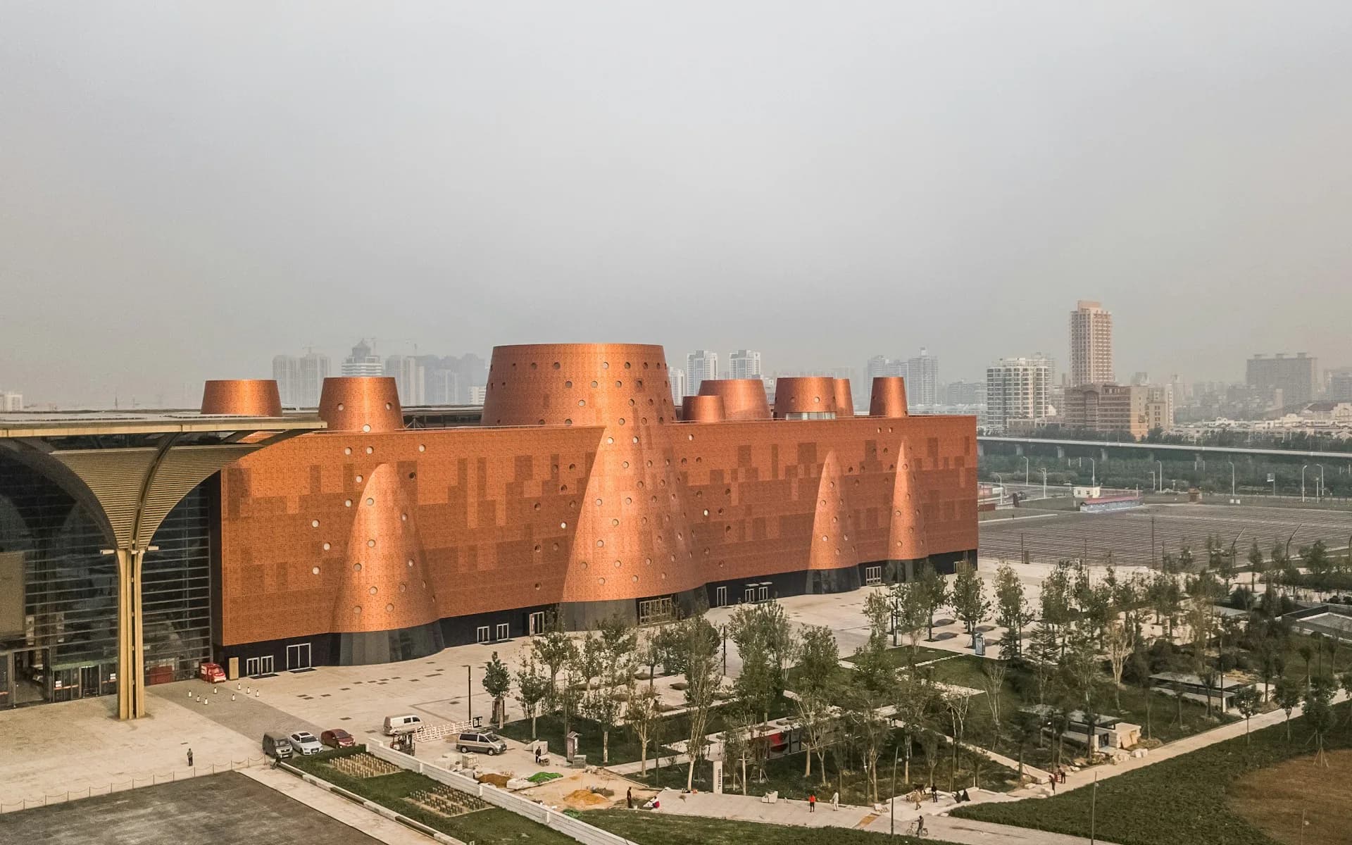 Expansive copper-clad cultural building with dramatic angular forms overlooking a landscaped plaza and waterfront cityscape by Bernard Tschumi Architects.