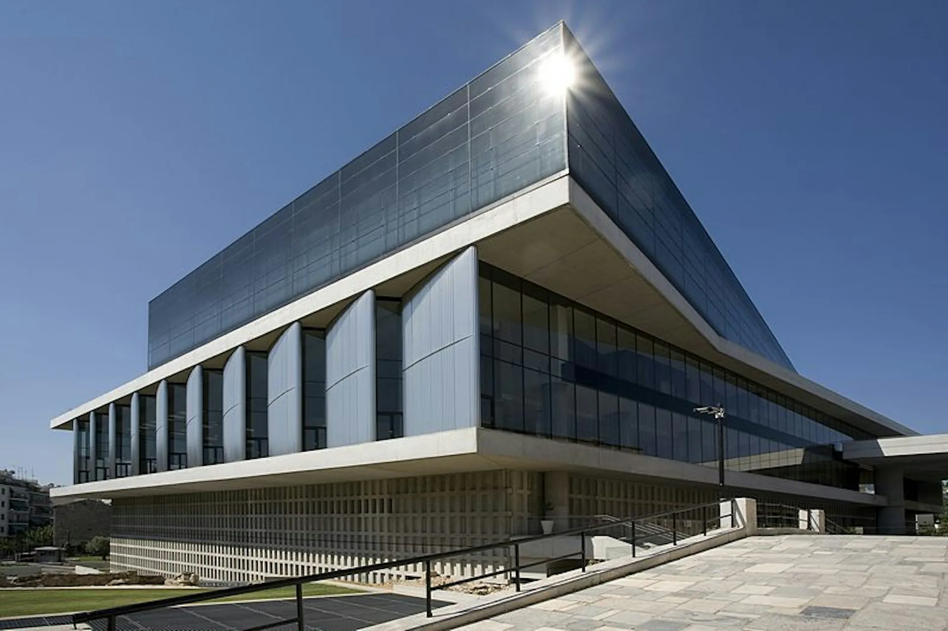 Modern institutional building with curved glass and metal facade, horizontal banding, and dramatic cantilever design against clear sky by Bernard Tschumi Architects.