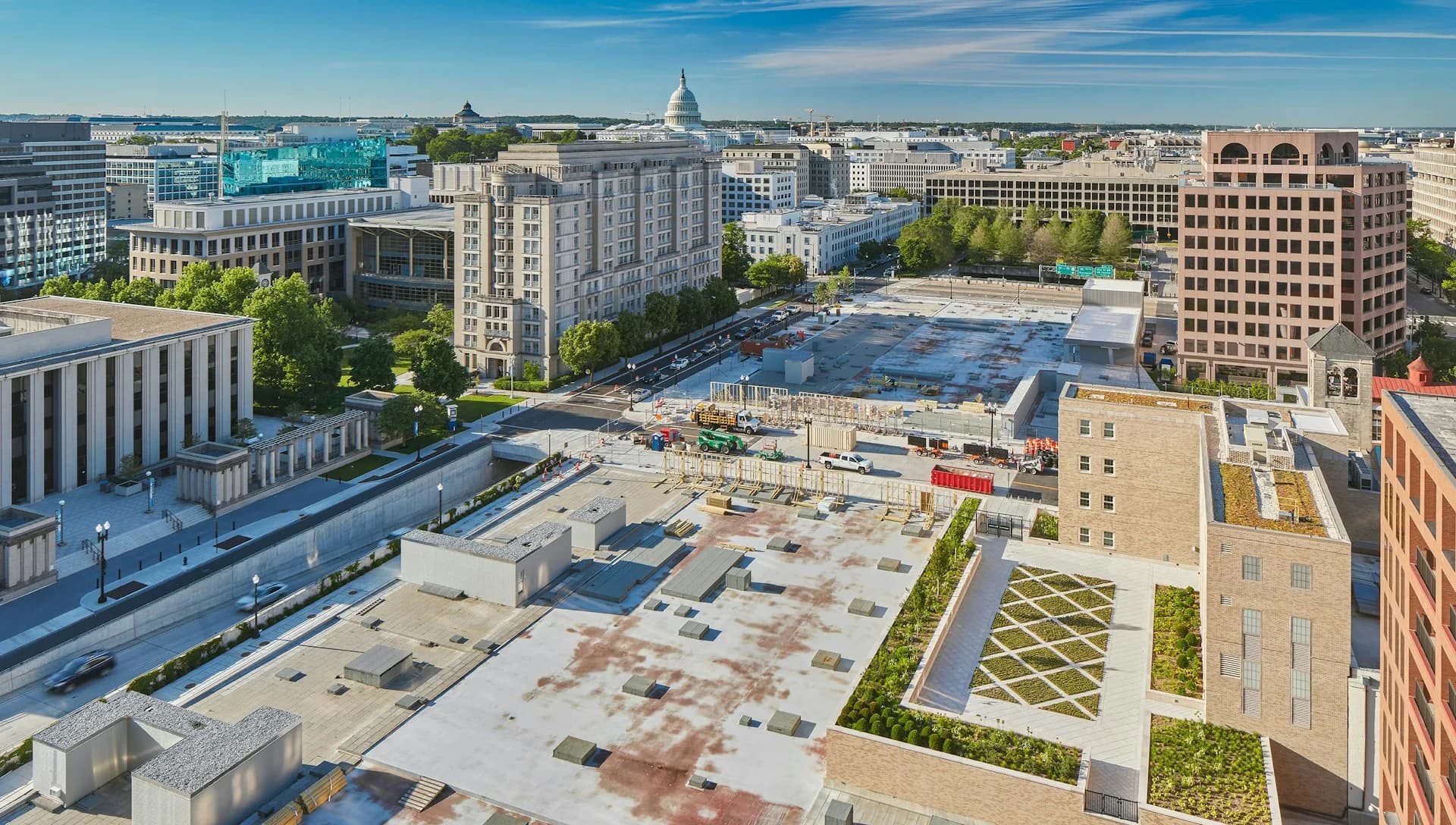 Aerial view of a mixed-use urban plaza with geometric hardscaping, green spaces, and surrounding historic and modern buildings with the Capitol visible in the distance by Beyer Blinder Belle.