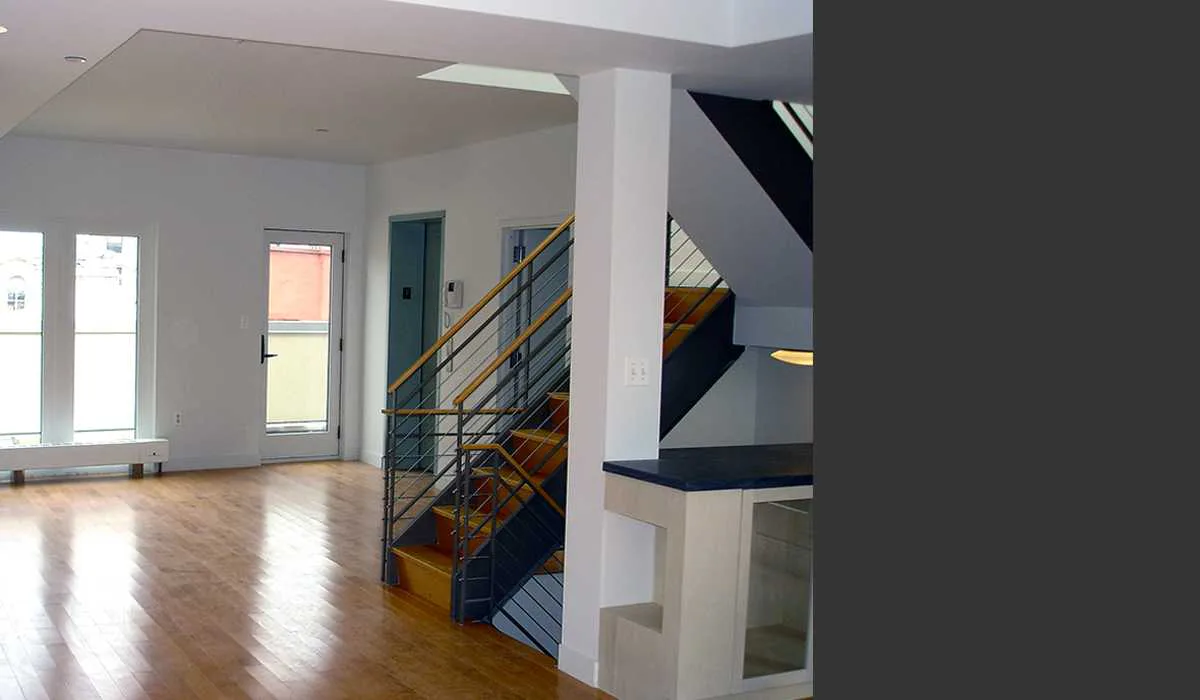 Modern loft interior with wooden flooring, white walls, steel and glass staircase with yellow accents, and natural light from large windows by Beyhan Karahan & Associates, Architects.