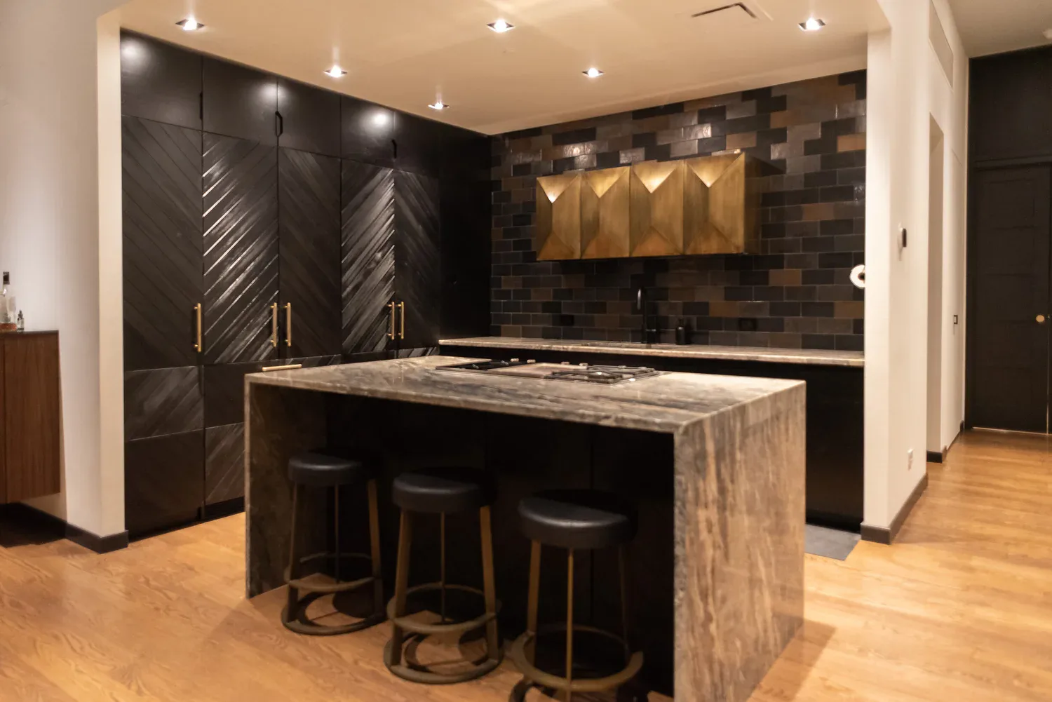 Modern kitchen with black cabinetry, marble waterfall island, brass hardware, and geometric tile backsplash by Bien Hecho.