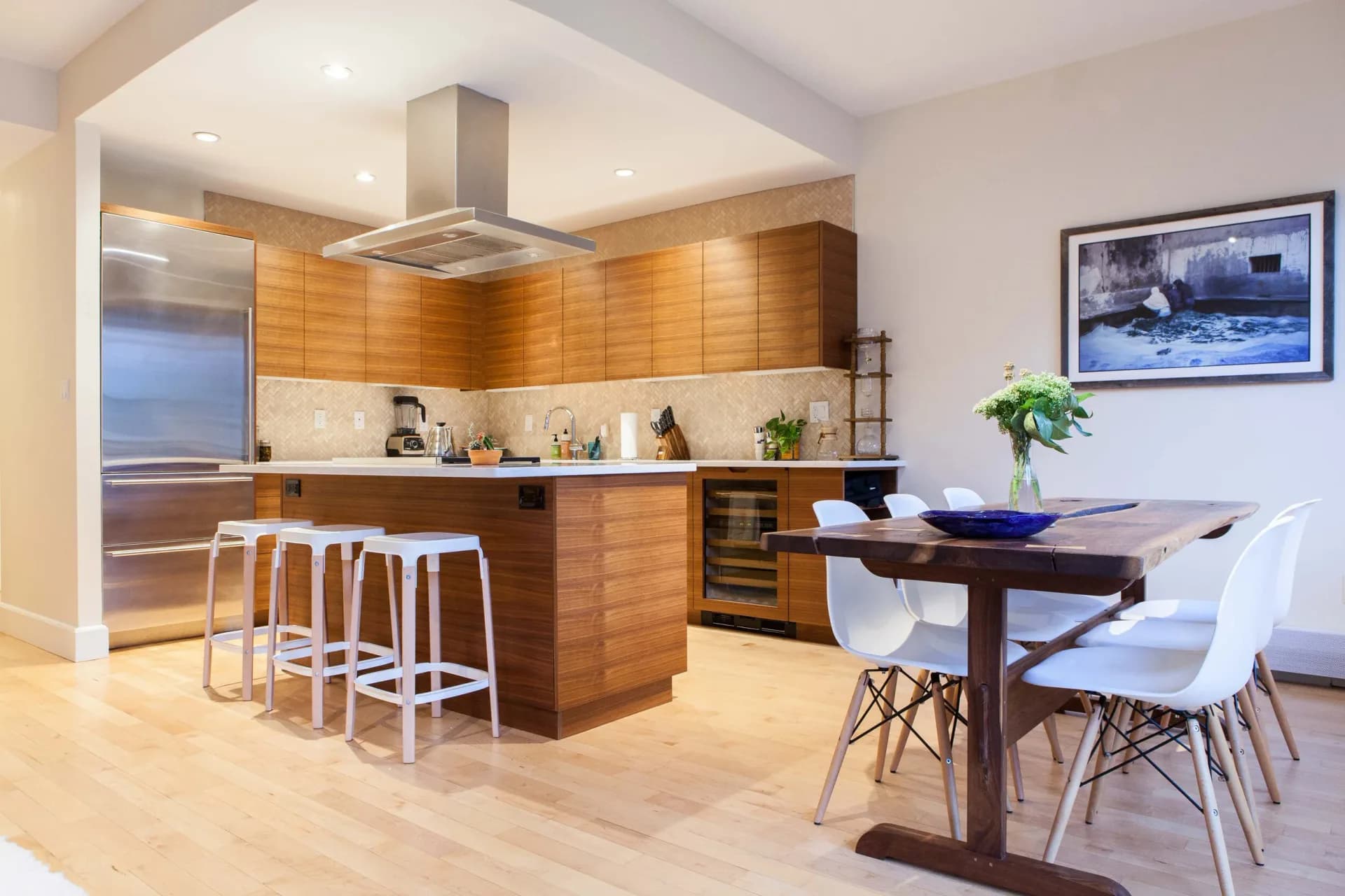 Modern open-plan kitchen and dining space with warm wood cabinetry, island seating, and contemporary furnishings by Bien Hecho, rendered with polished materials and synthetic lighting.