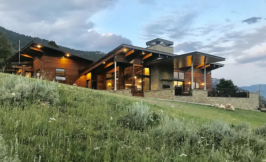 Modern residential architecture with wood and stone exterior nestled in mountainous landscape with native grasses by Bitnar Architects.