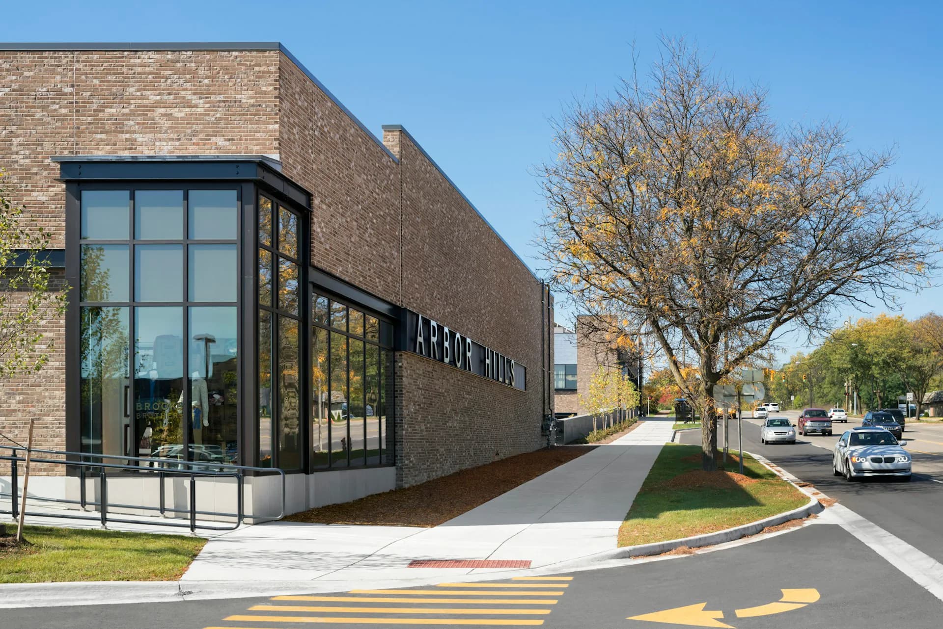Modern brick institutional building with corner glass facade, clean walkway with yellow striping, and mature trees along street by BKSK Architects.