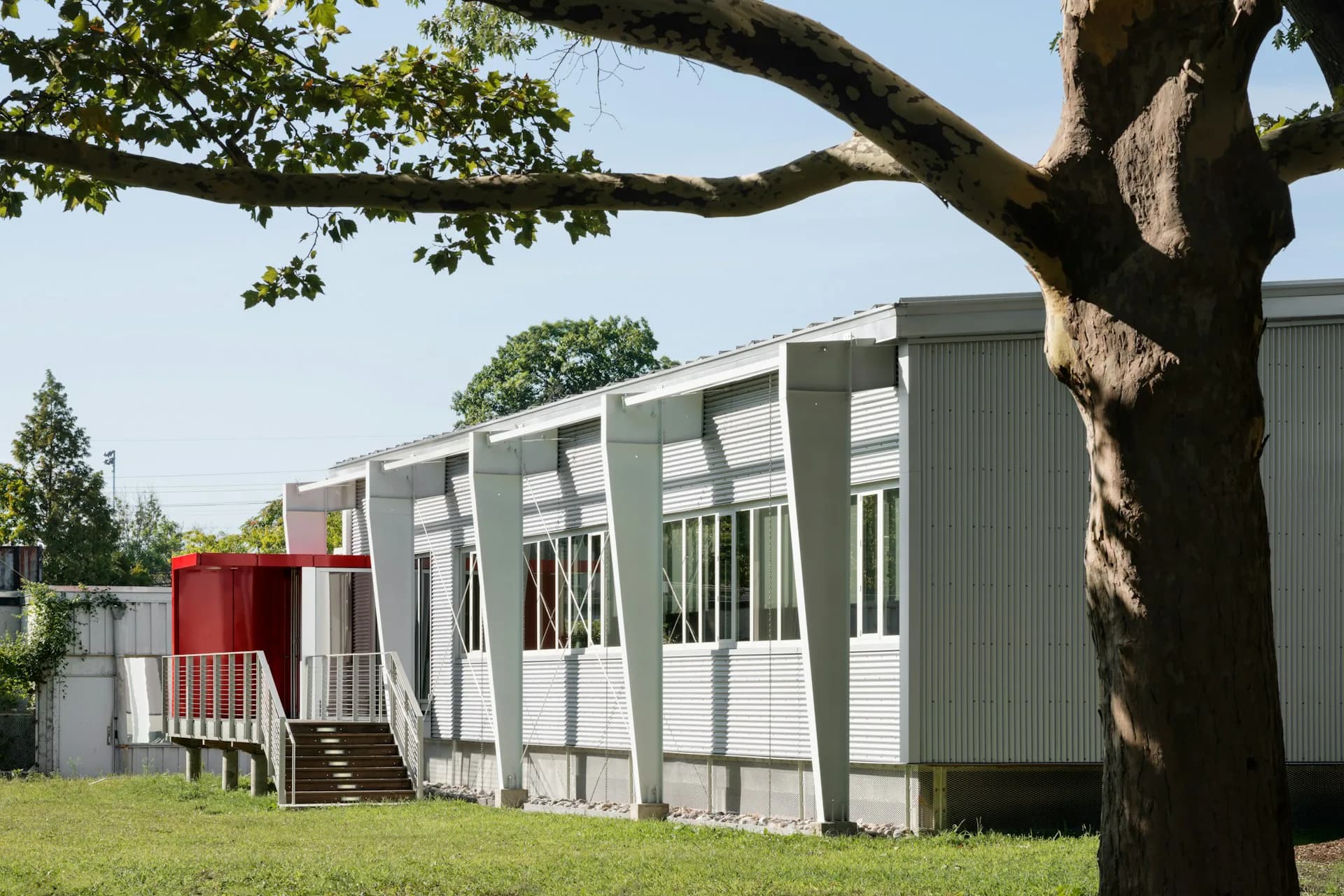 Modern modular building with white and green corrugated metal exterior set in a grassy landscape beneath mature trees, by BKSK Architects.
