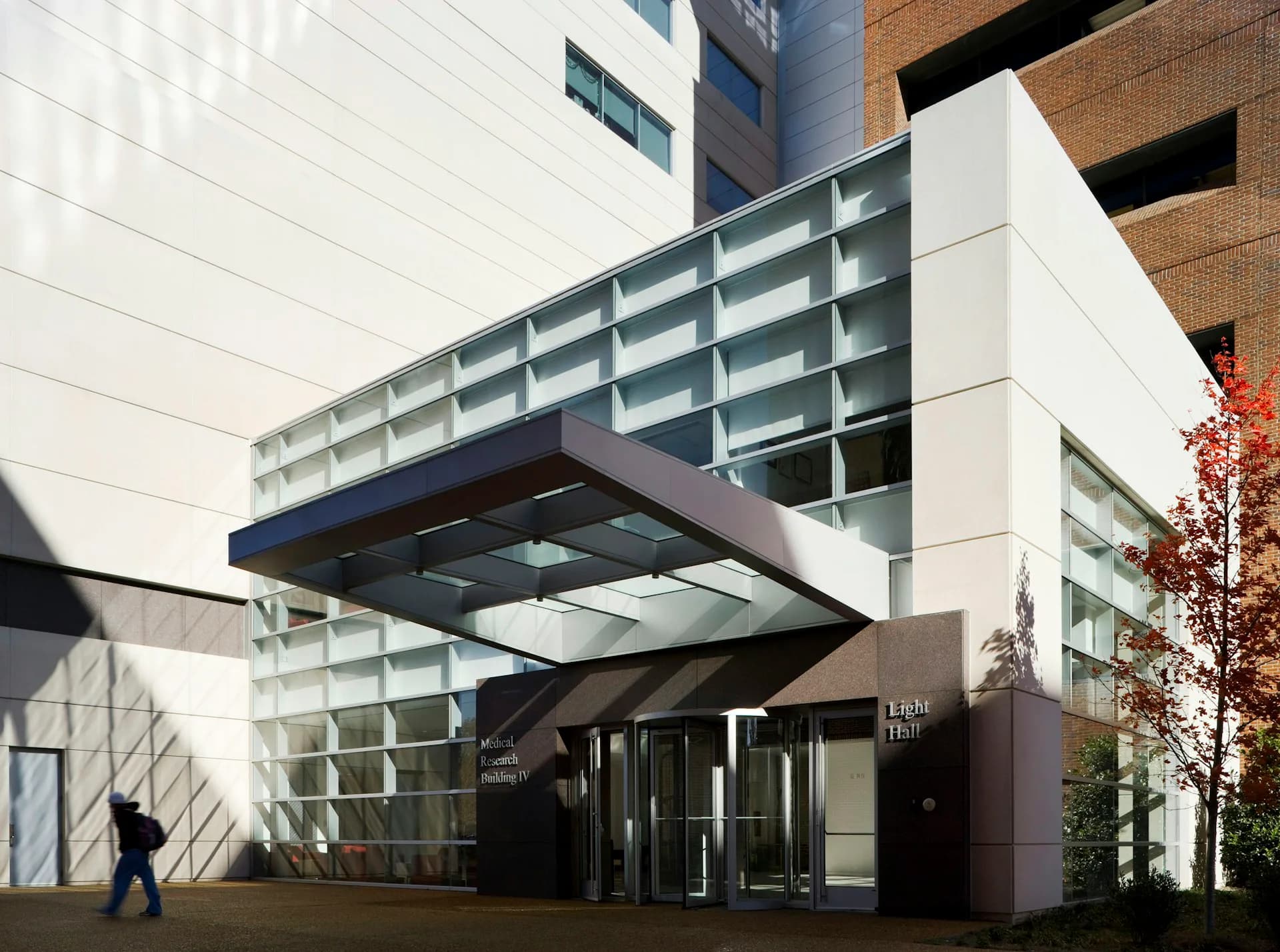 Contemporary institutional building entrance with cantilevered steel and glass structures, white and brick facades, and minimalist dark entrance pavilion by Blair + Mui Dowd Architects.