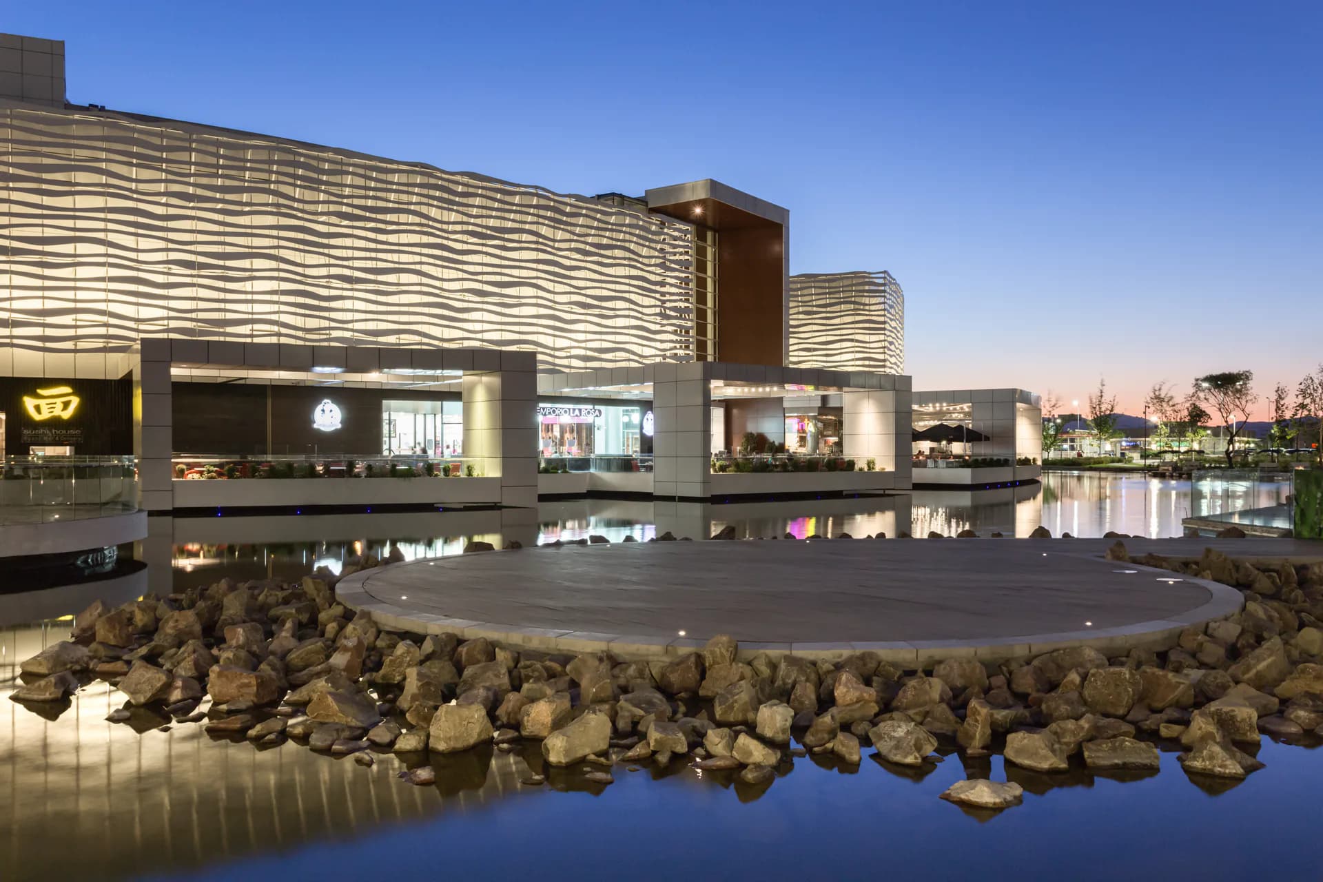 Modern waterfront museum with striped facade and dramatic cantilevered design reflected in still water, surrounded by rocky landscape by Bliss Fasman.