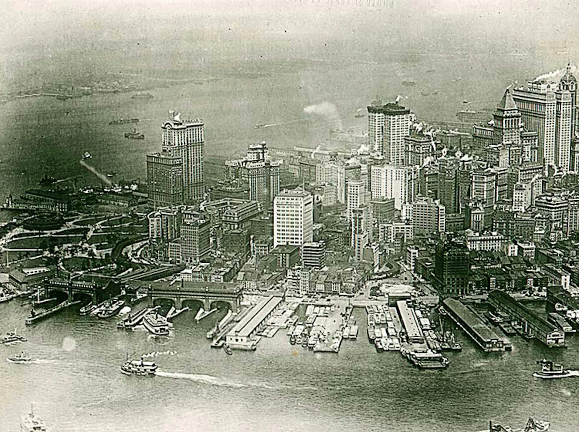 Aerial cityscape photograph of downtown Manhattan waterfront with high-rise buildings and docked ships along the harbor, showing urban density and architectural scale by Bone/Levine Architects.