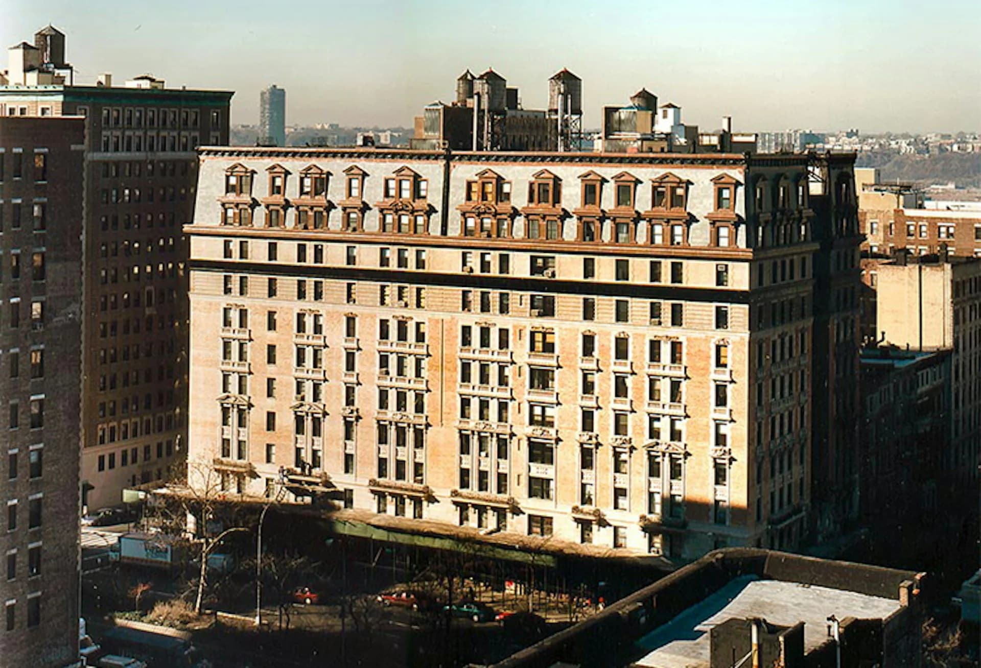 Cream-colored Art Deco residential building with regular window patterns and ornamental roofline detail, set among darker surrounding buildings in an urban cityscape by Bone/Levine Architects.