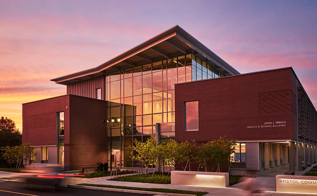 Modern institutional building with red brick facade and extensive glazing at dusk, featuring dramatic angled roofline and warm interior lighting by Borealis Lighting Studio (BR+A Consulting Engineers).