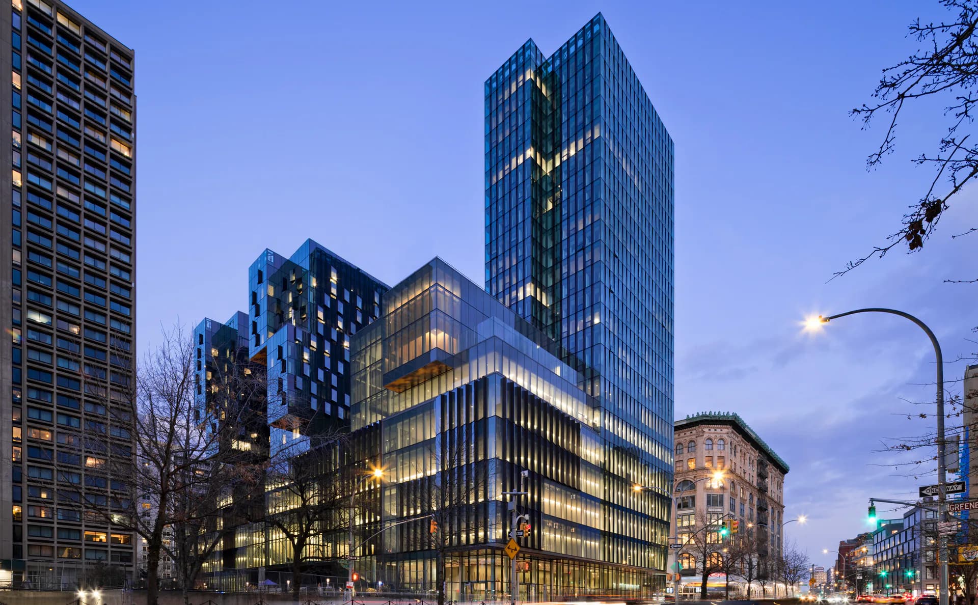 Urban streetscape at dusk featuring illuminated multi-story office and residential buildings with warm interior lighting and architectural accent lighting by Borealis Lighting Studio (BR+A Consulting Engineers).