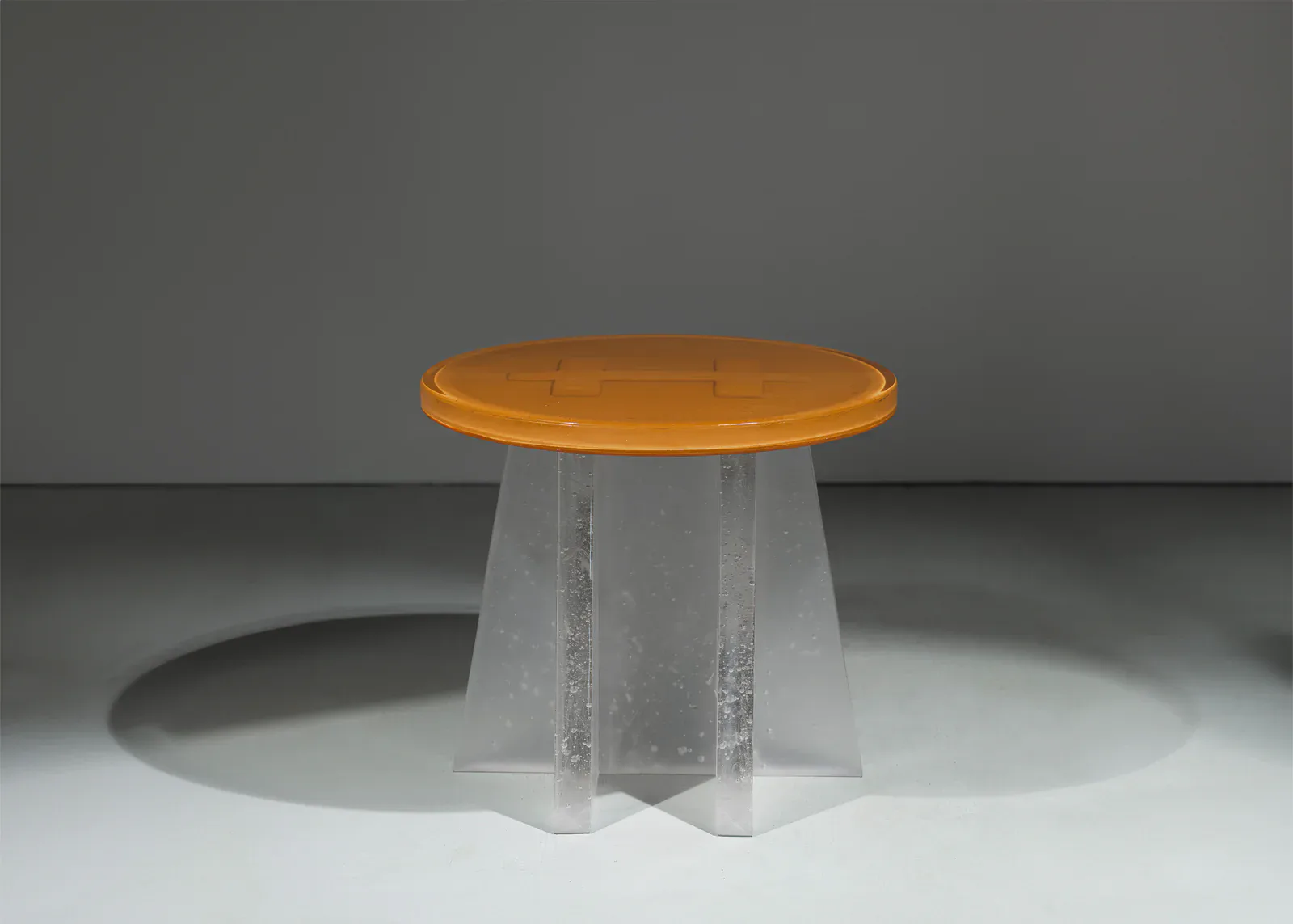 A modernist table design with a translucent frosted glass conical base and bright orange circular top, displayed in a minimalist studio setting by Bowen Liu Studio.