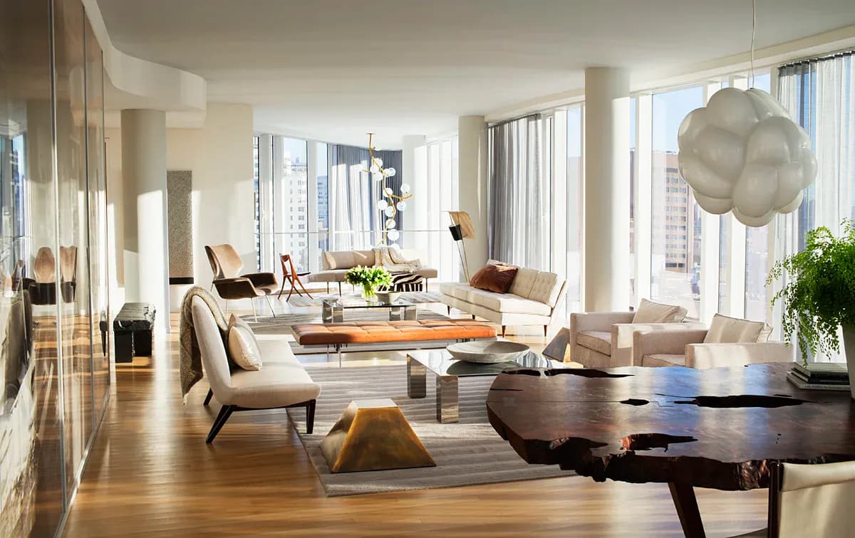 Modern luxury living room with cream seating, dark wood tables, floor-to-ceiling windows, and sculptural pendant lighting by Brad Ford ID.