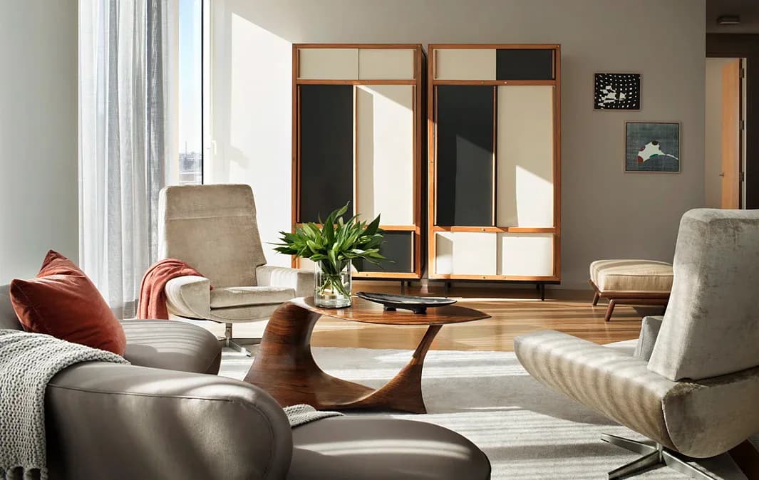 Modern living room with curved furniture, wood-framed mirrors, neutral palette, and natural light by Brad Ford ID.