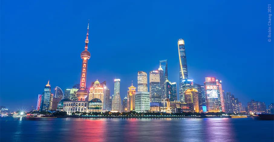 Shanghai skyline at dusk with illuminated skyscrapers reflected in water, showcasing architectural and lighting design by Brandston Partnership Inc.