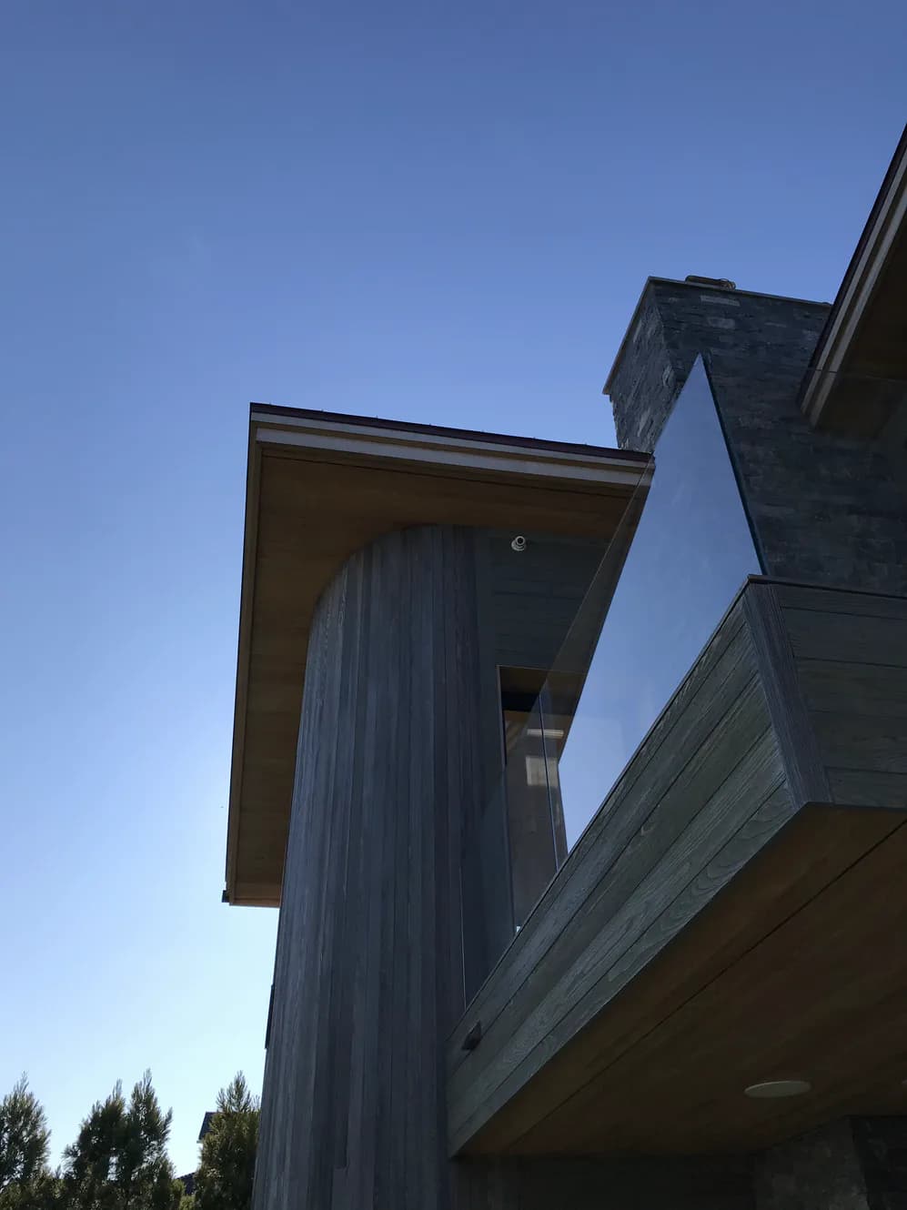 Modern residential architecture featuring a vertical metal-clad tower element with geometric concrete overhangs against a clear blue sky, by Buck Moorhead Architect.