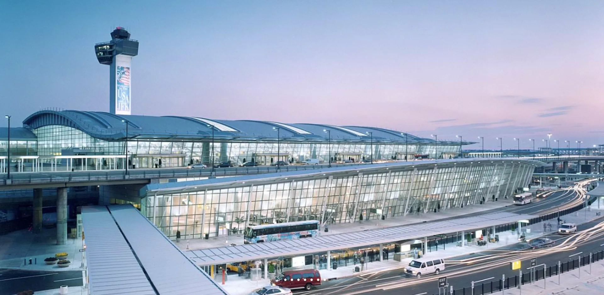 Modern airport terminal with curved glass facade and control tower at dusk, featuring expansive architectural design by CallisonRTKL.