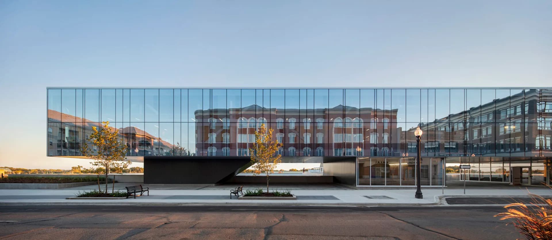 Modern waterfront plaza with reflective black pavilion structure and glass barriers overlooking water and historic buildings at dusk by CannonDesign.