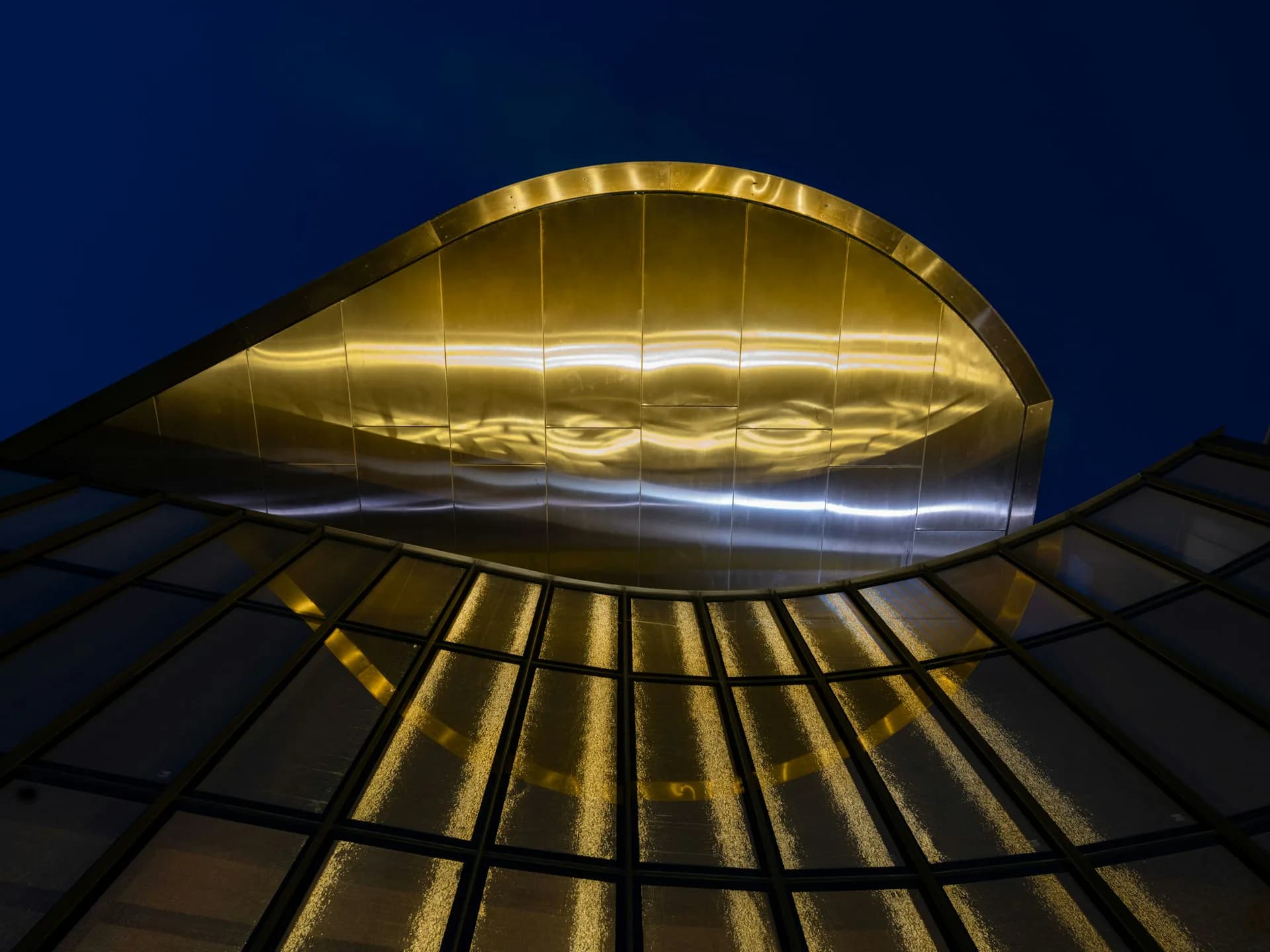 Illuminated golden architectural canopy with ribbed structural details photographed at dusk against a dark blue sky, by Caples Jefferson Architects.