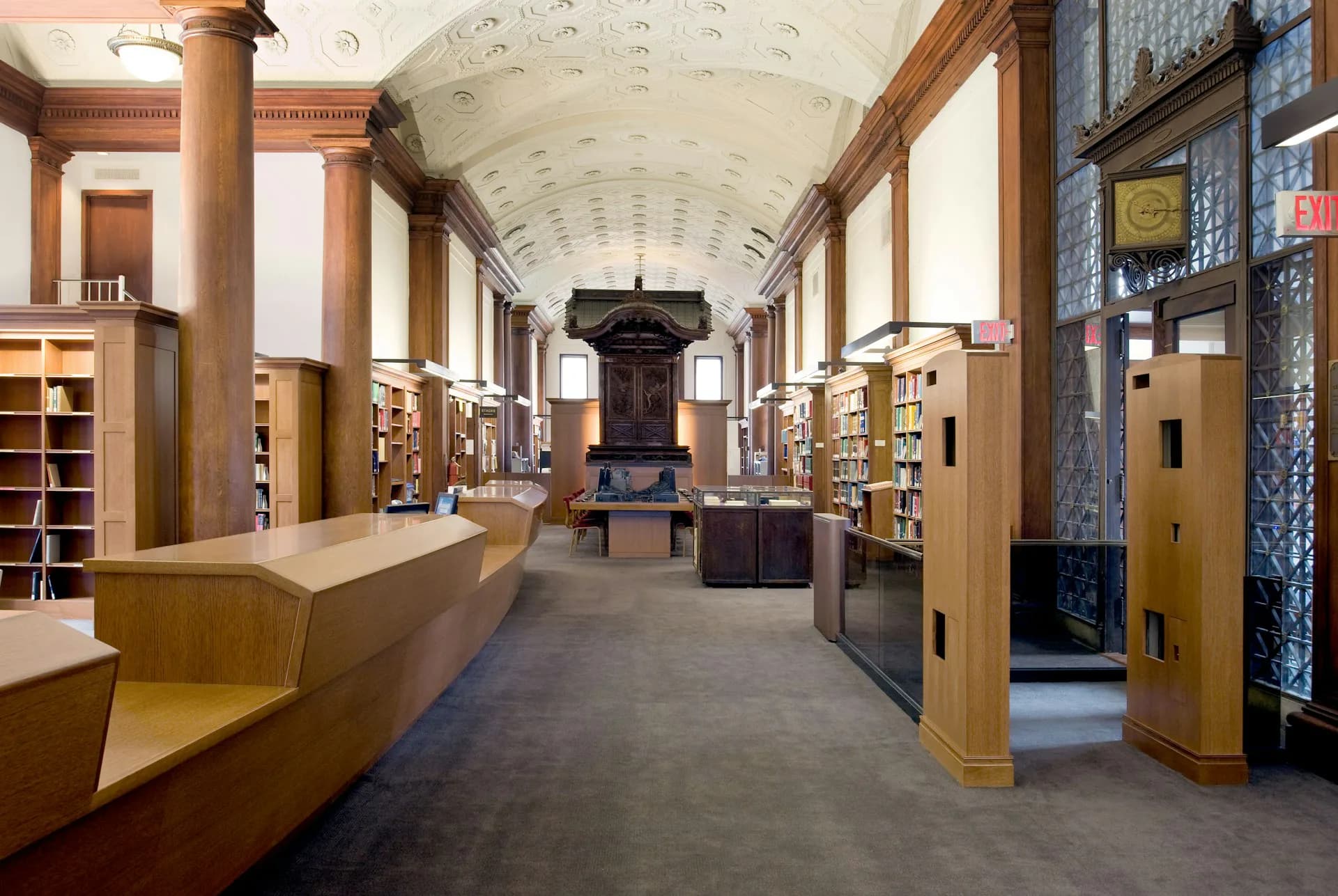 A modern library interior with a barrel-vaulted ceiling, wooden cabinetry, columns, and a central desk, designed by Caples Jefferson Architects.