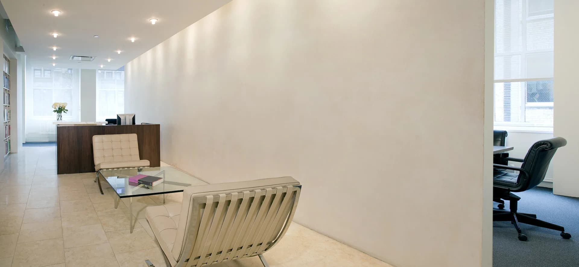Modern office reception area featuring minimalist design with cream-colored walls, polished concrete flooring, and contemporary furniture including a woven lounge chair by Carlton Architecture PC.