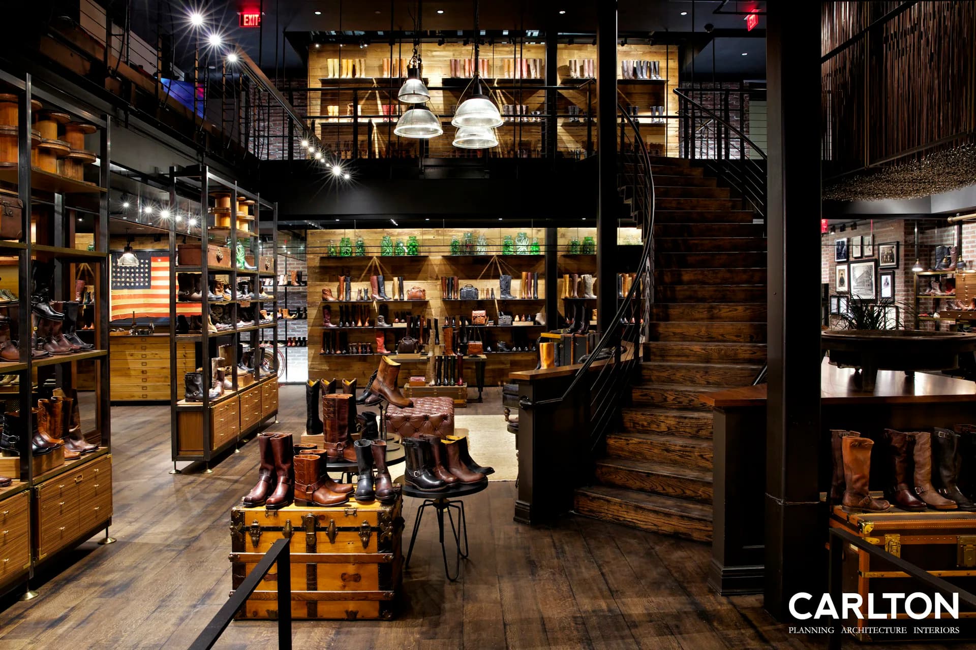 Warm-toned retail interior with wooden fixtures, shelving, and display tables, featuring industrial elements and ambient lighting throughout the space by Carlton Architecture PC.