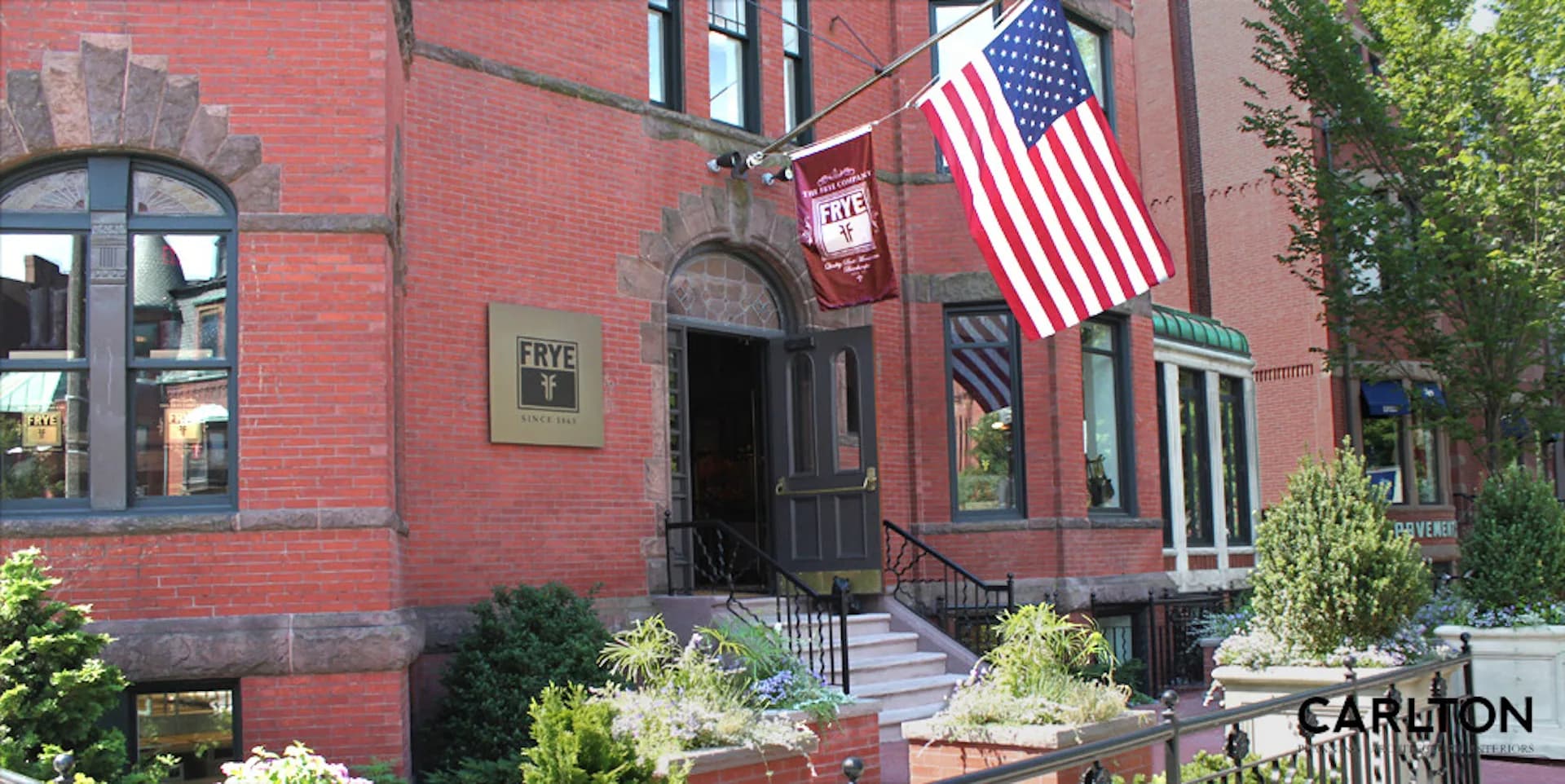 Red brick historic building facade with arched windows, black railings, and American flag, landscaped entry by Carlton Architecture PC.
