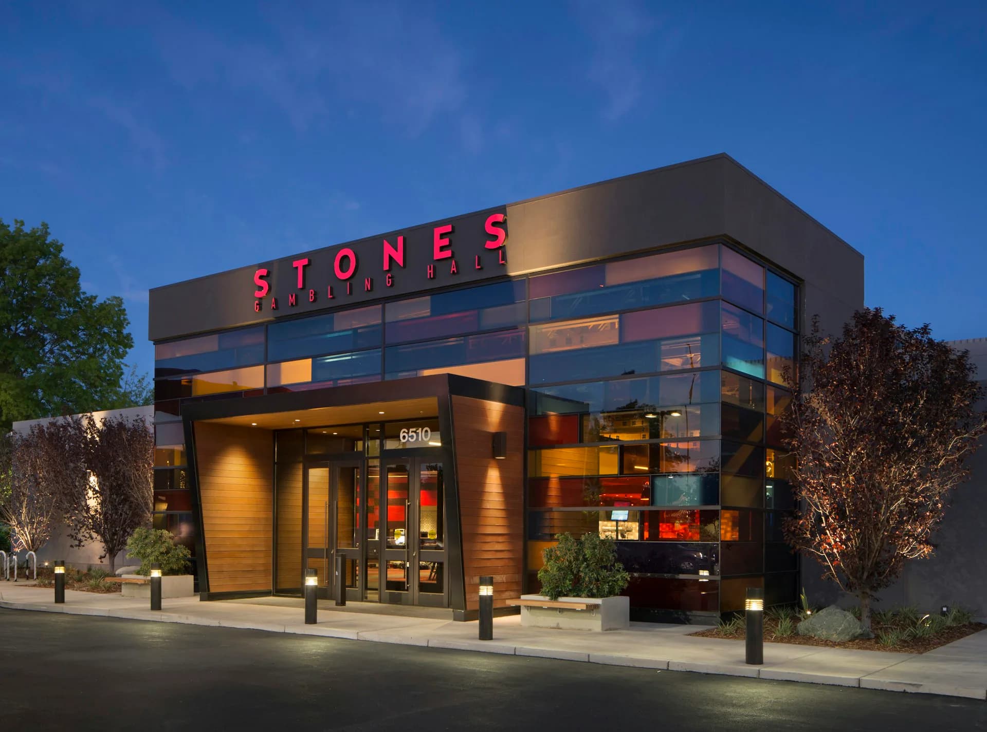 Modern Stones restaurant exterior at dusk featuring angular architecture with dark metal cladding, illuminated window displays, and warm accent lighting, designed by Cass Calder Smith Architecture + Interiors.
