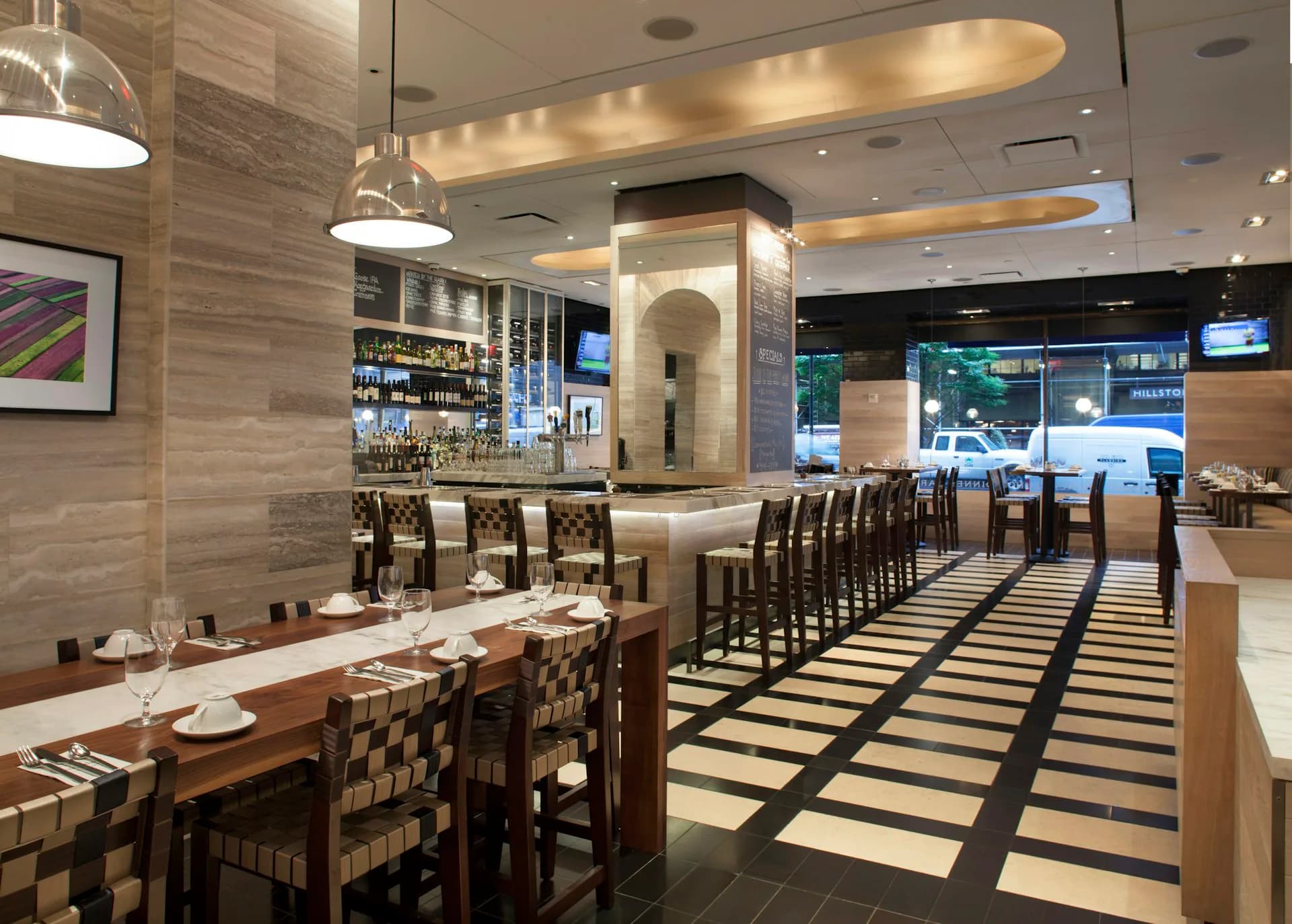 Modern restaurant interior with warm wood and stone finishes, geometric black-and-white flooring, pendant lighting, bar seating, and dining areas with contemporary furnishings by Cass Calder Smith Architecture + Interiors.