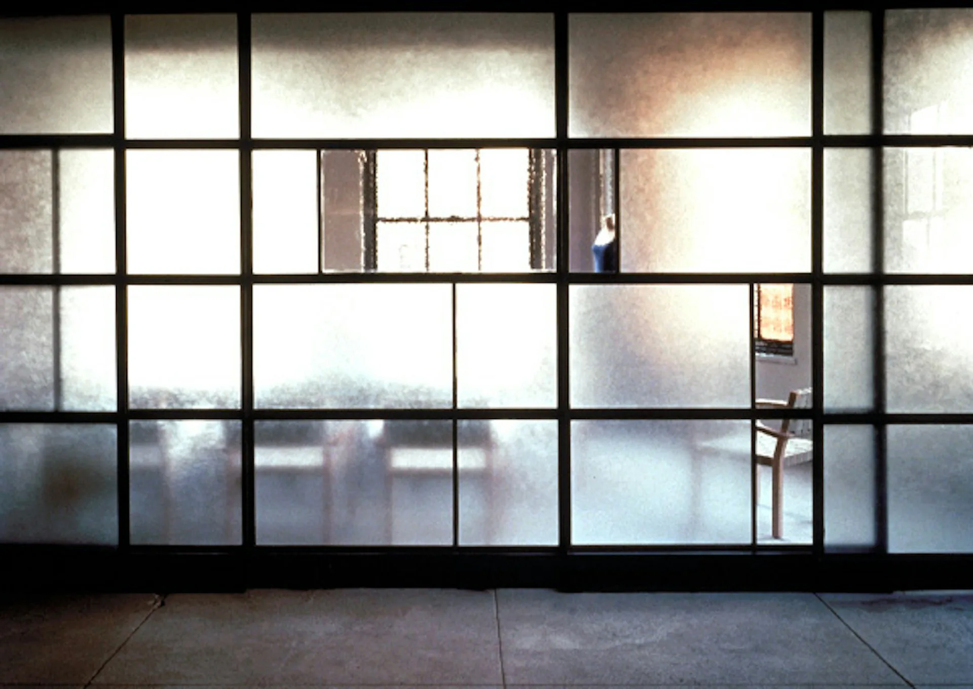 Modern interior with expansive gridded black-framed windows overlooking a cityscape, concrete flooring, and minimalist aesthetic by CDR Studio Architects, PC.