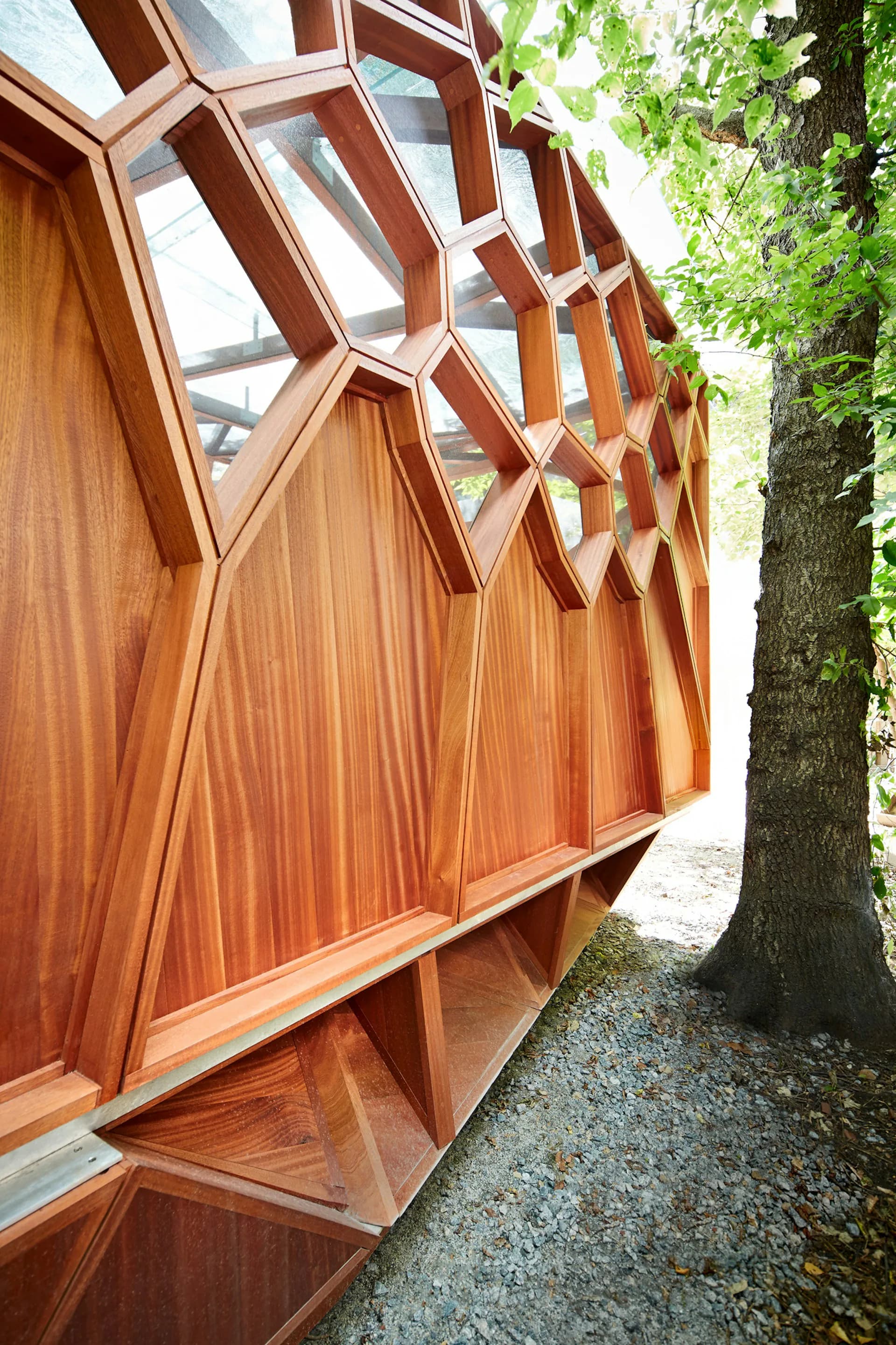 Exterior detail of a wooden architectural structure with geometric lattice windows and vertical paneling, situated beside ivy-covered trees by CDR Studio Architects, PC.