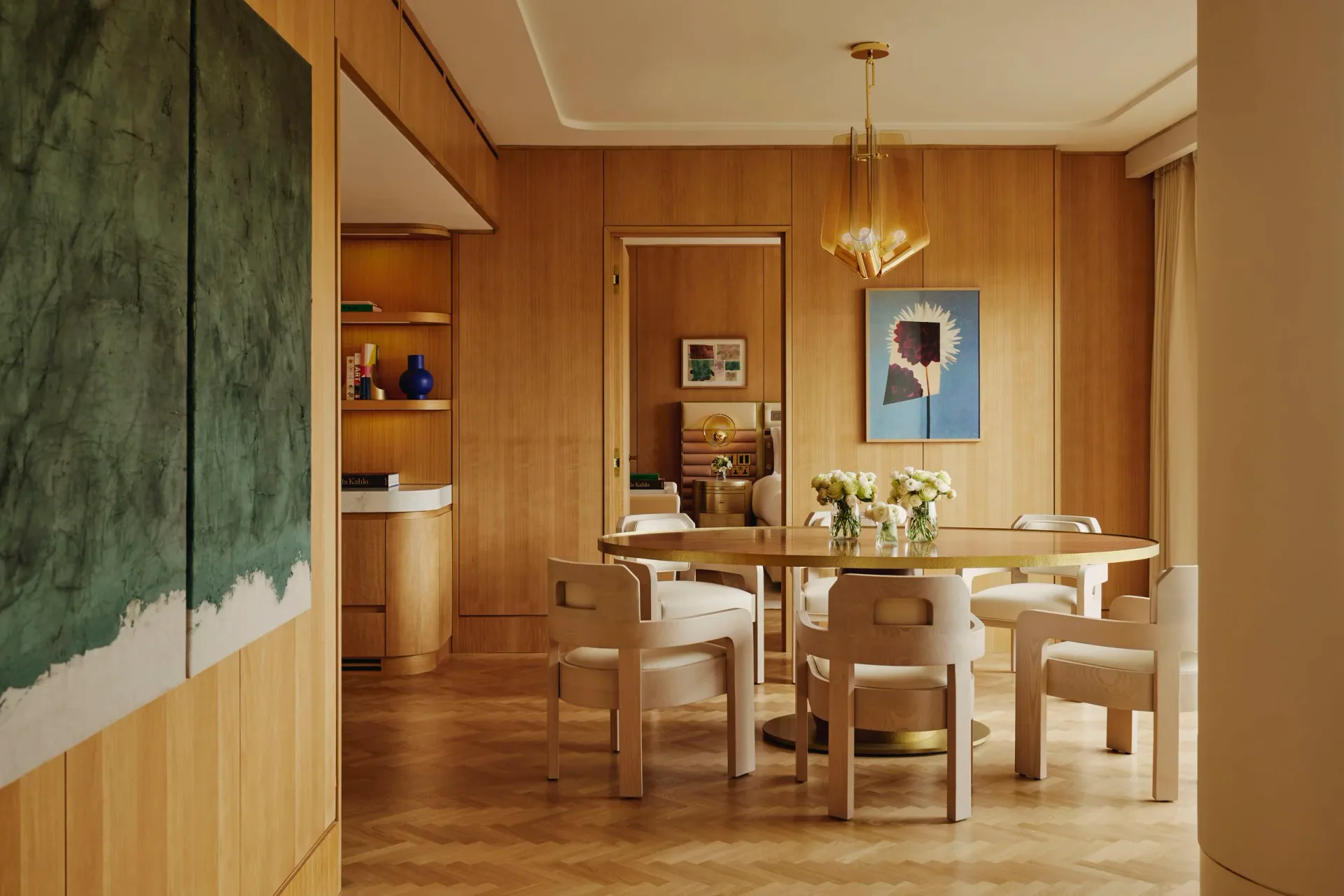 Warm wood-paneled dining space with natural light, featuring a wooden table, upholstered chairs, and modern artwork by Champalimaud Design.