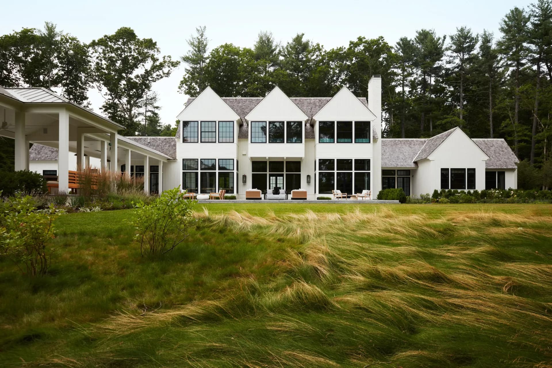 Modern white farmhouse with glass and black trim set in a grassy landscape with mature trees, designed by Chango & Co.