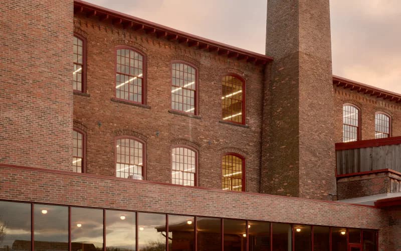 Brick industrial building facade with large windows and modern glass storefront entrance at dusk, designed by Charlap Hyman & Herrero.