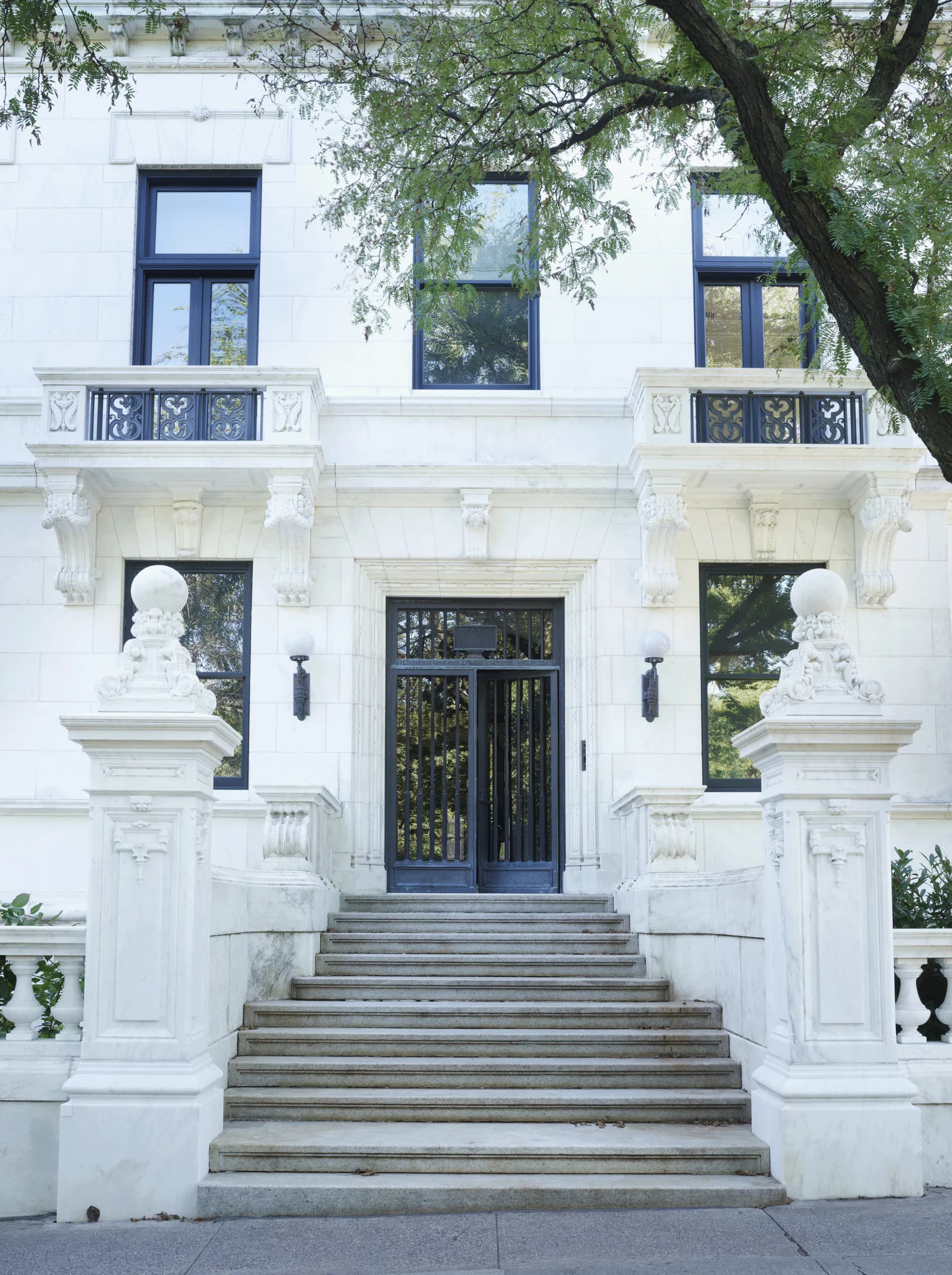 Neoclassical white facade with symmetrical stone busts, grand entrance stairs, black doors, and ornate balconies by Charlotte Worthy Architects.